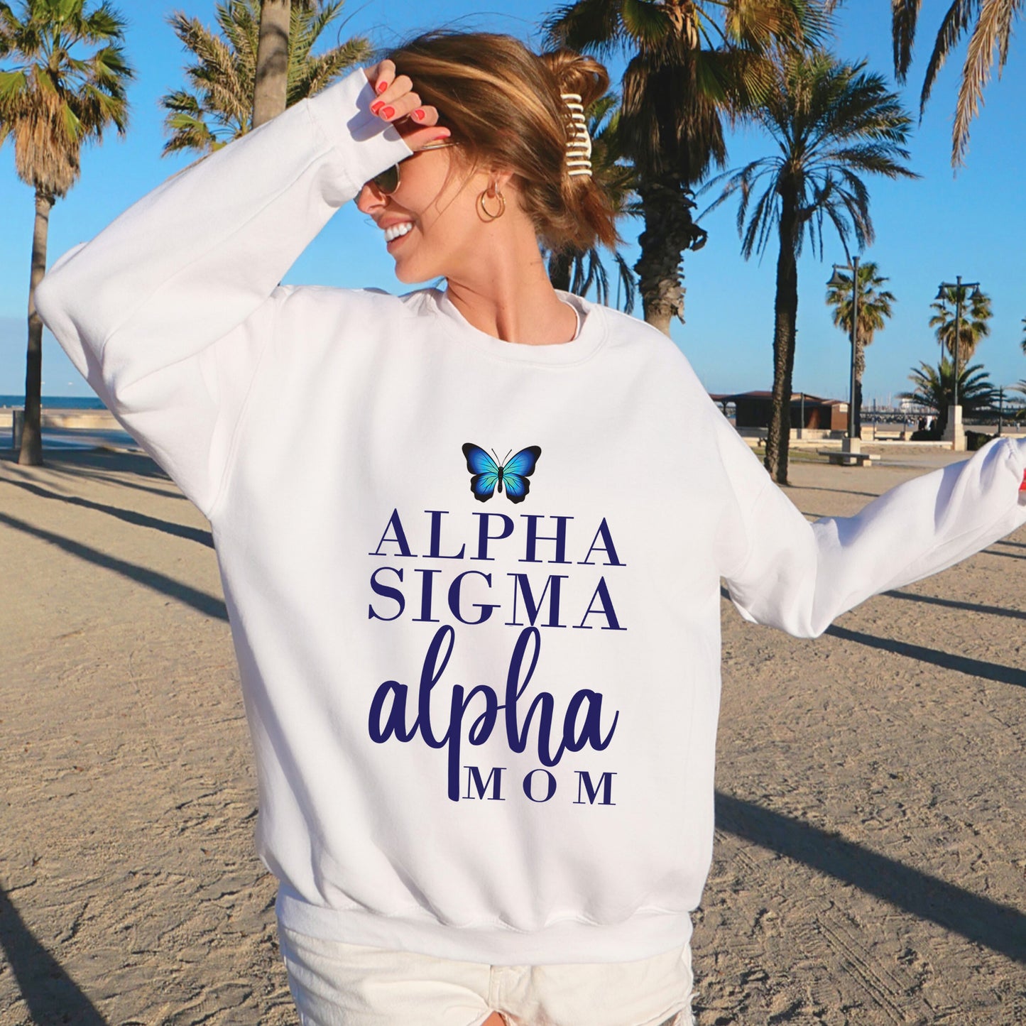 a woman standing on a beach wearing a white sweatshirt