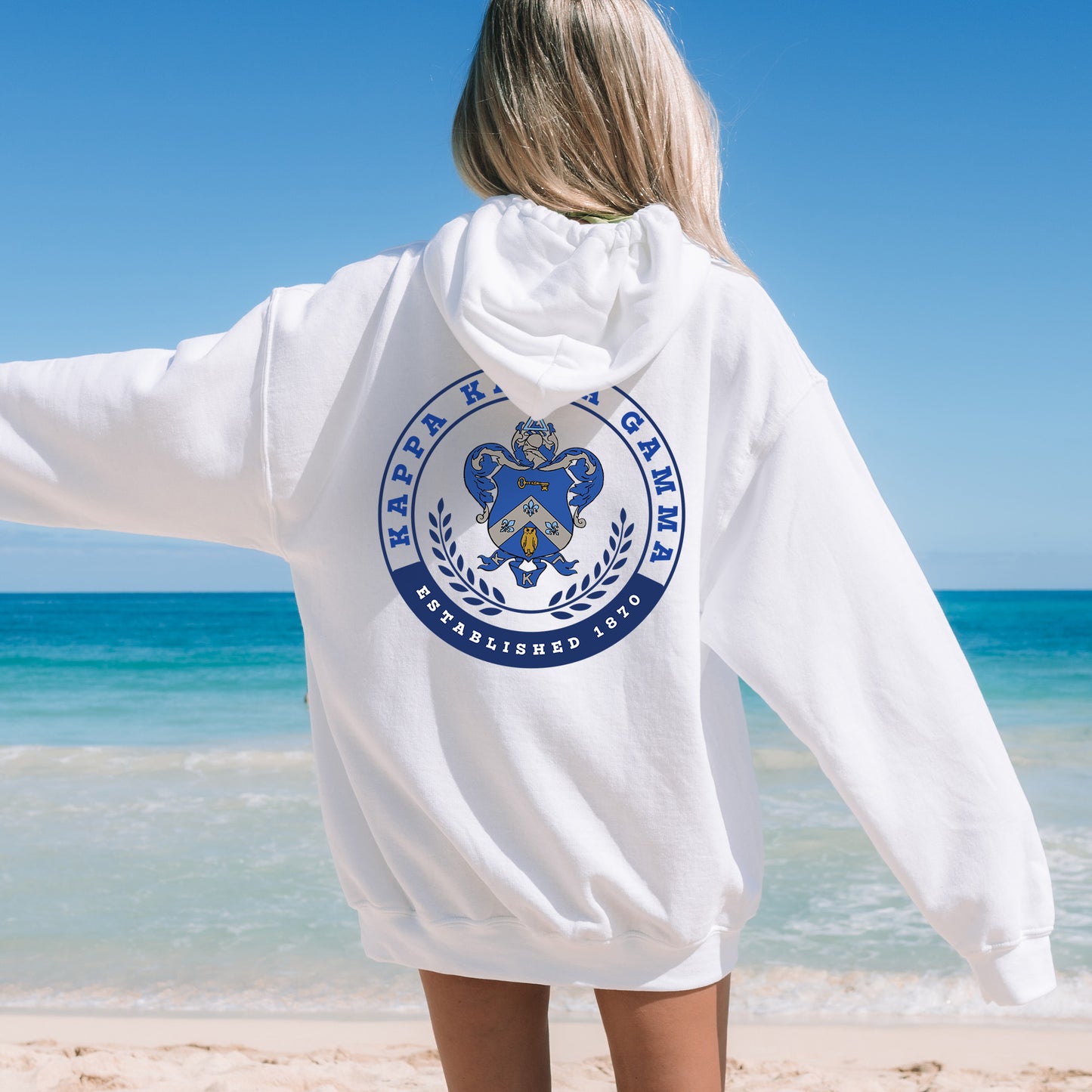 a woman standing on a beach wearing a white hoodie