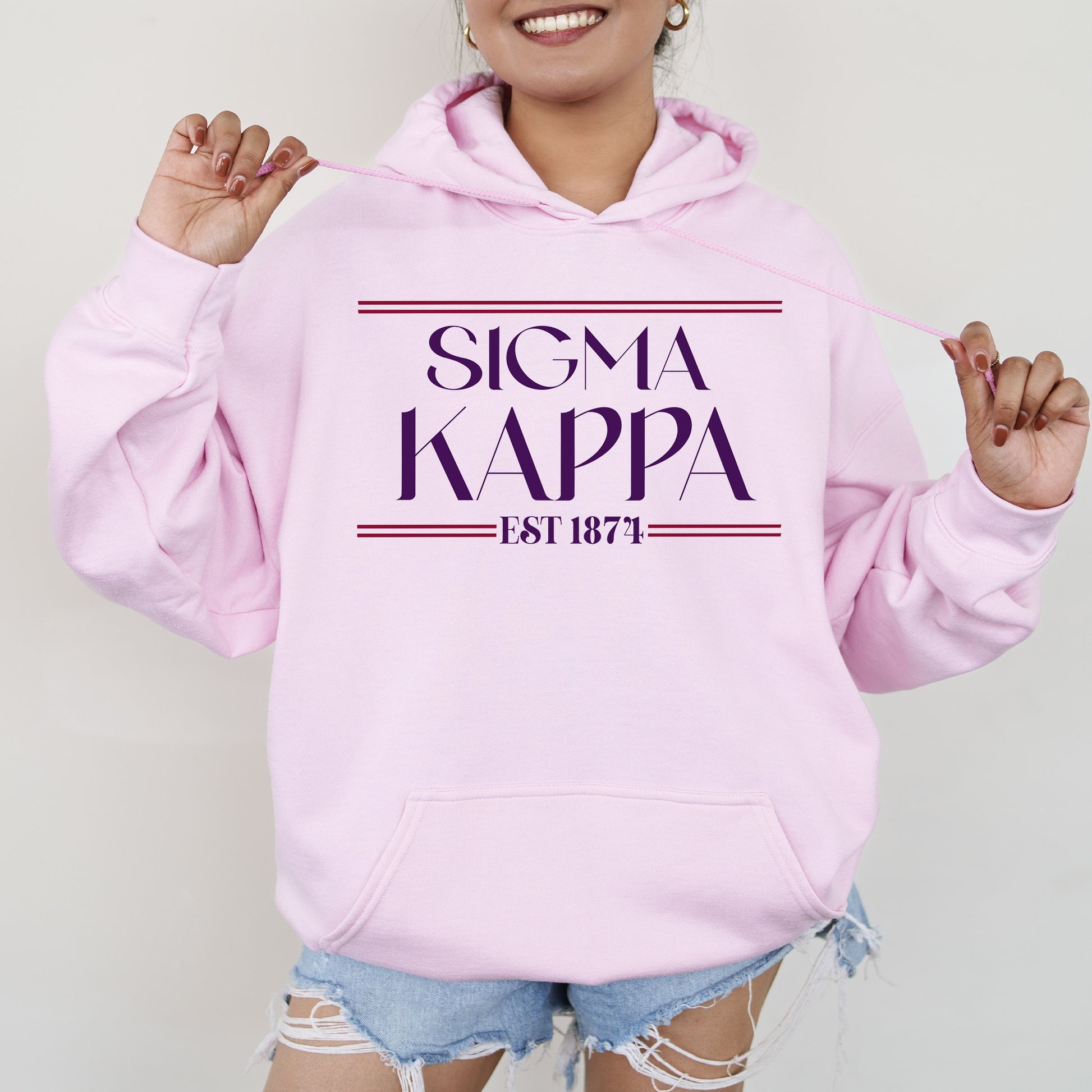 a woman wearing a pink hoodie with the word sigma kappa printed on