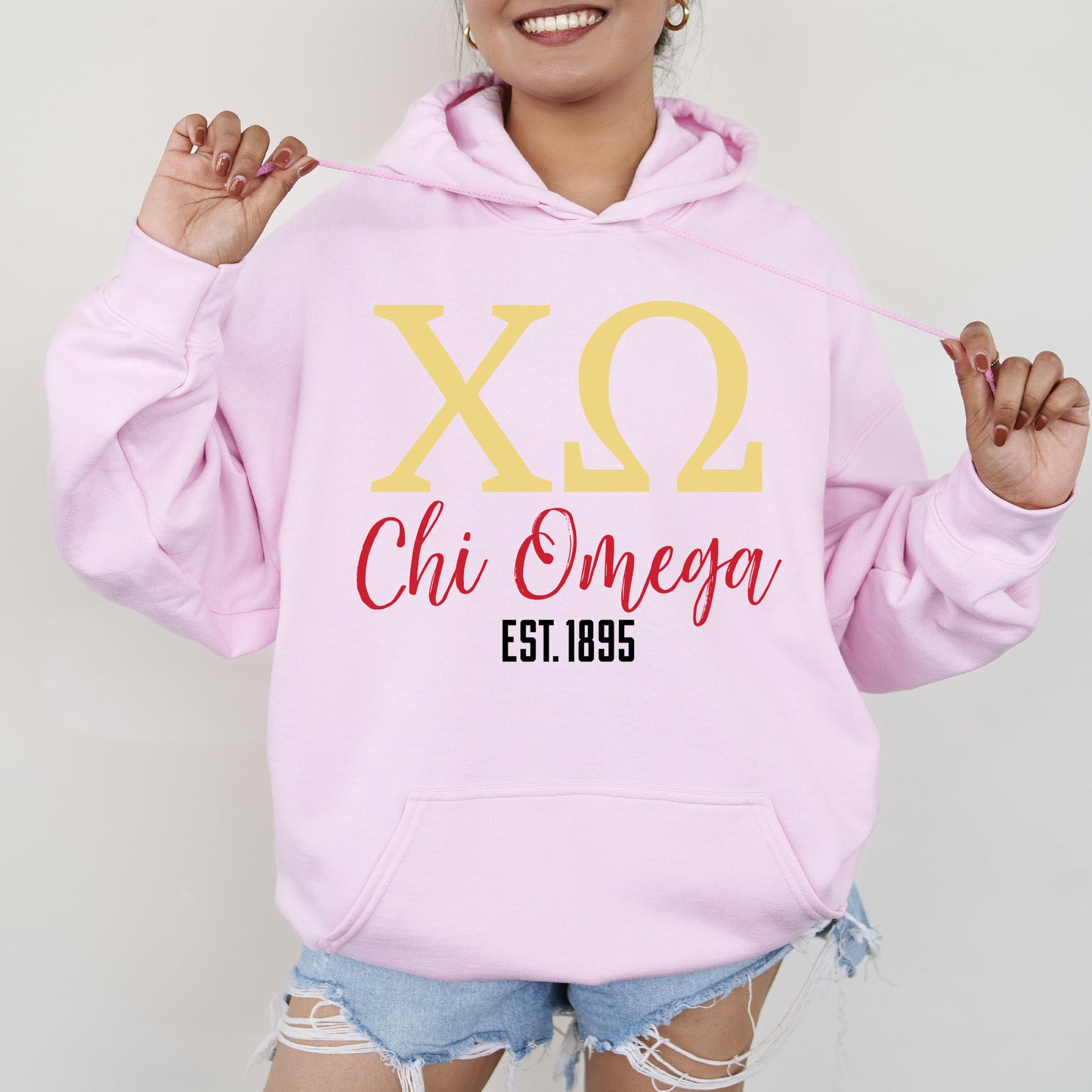 a woman wearing a pink hoodie that says xo chi omega est