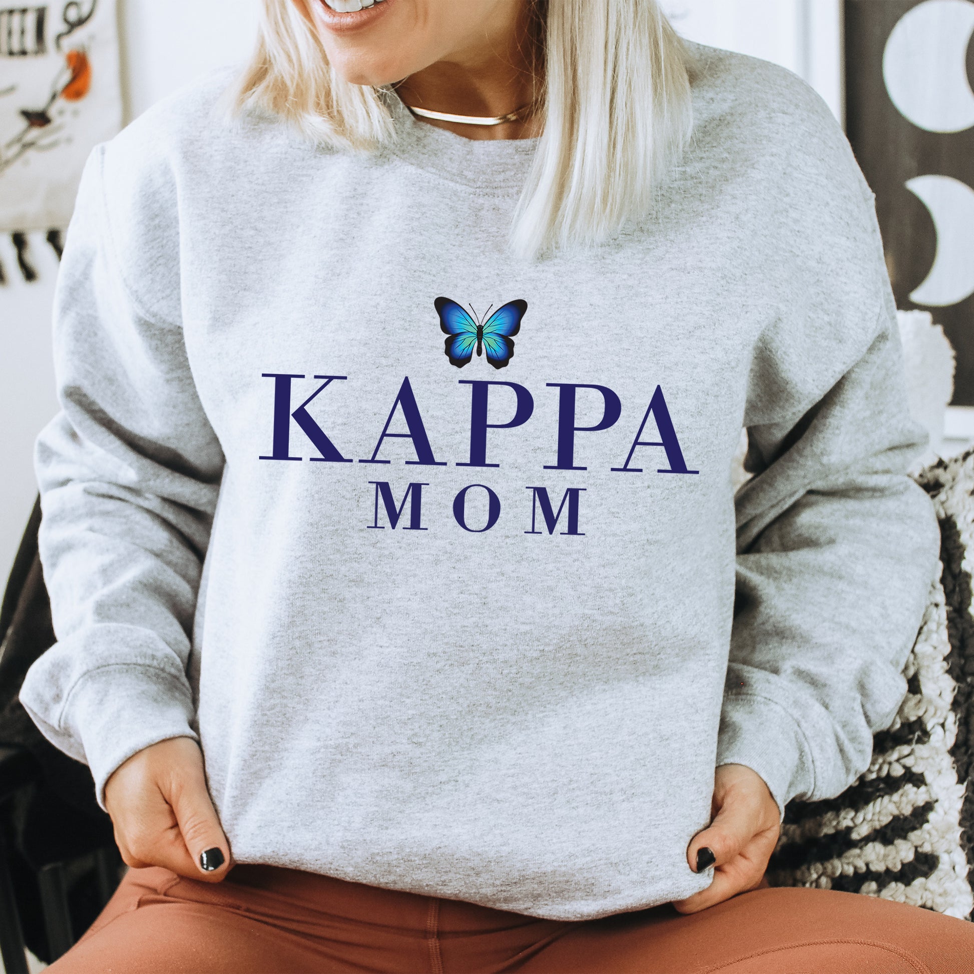 a woman sitting on a chair wearing a sweatshirt that says kappa mom