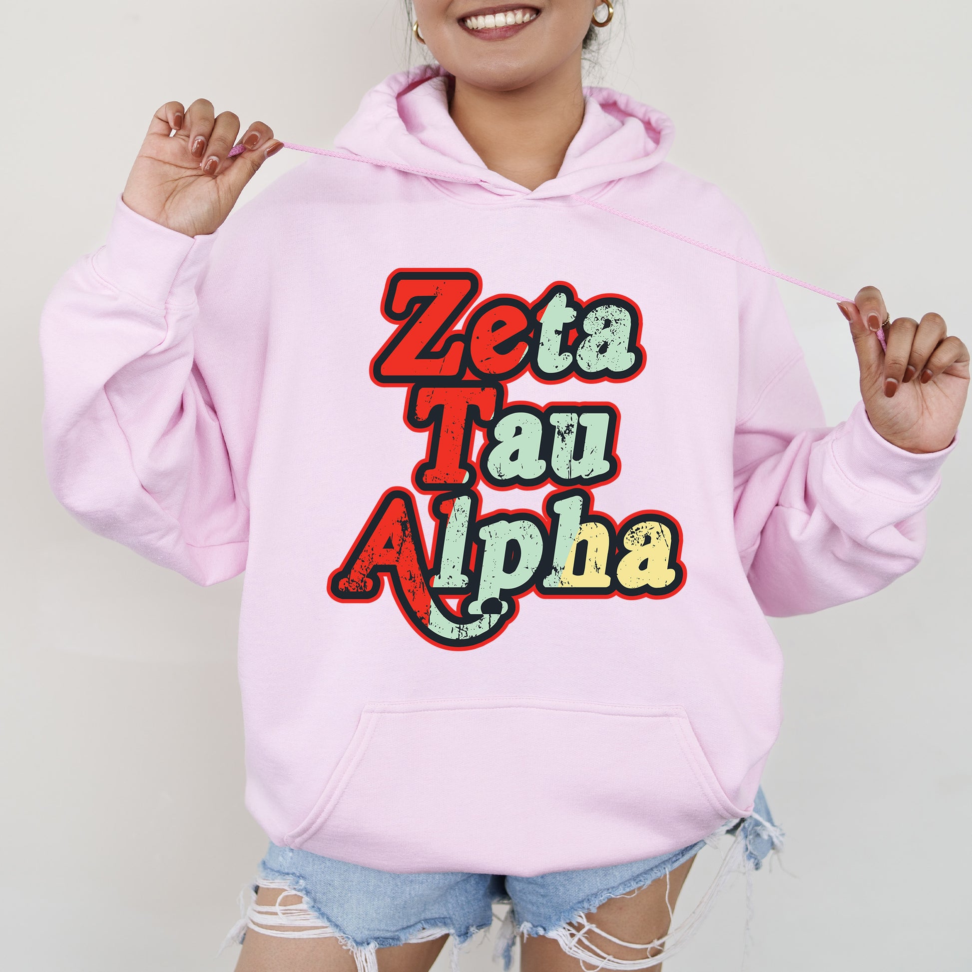 a woman wearing a pink hoodie that says zeta tau alpha