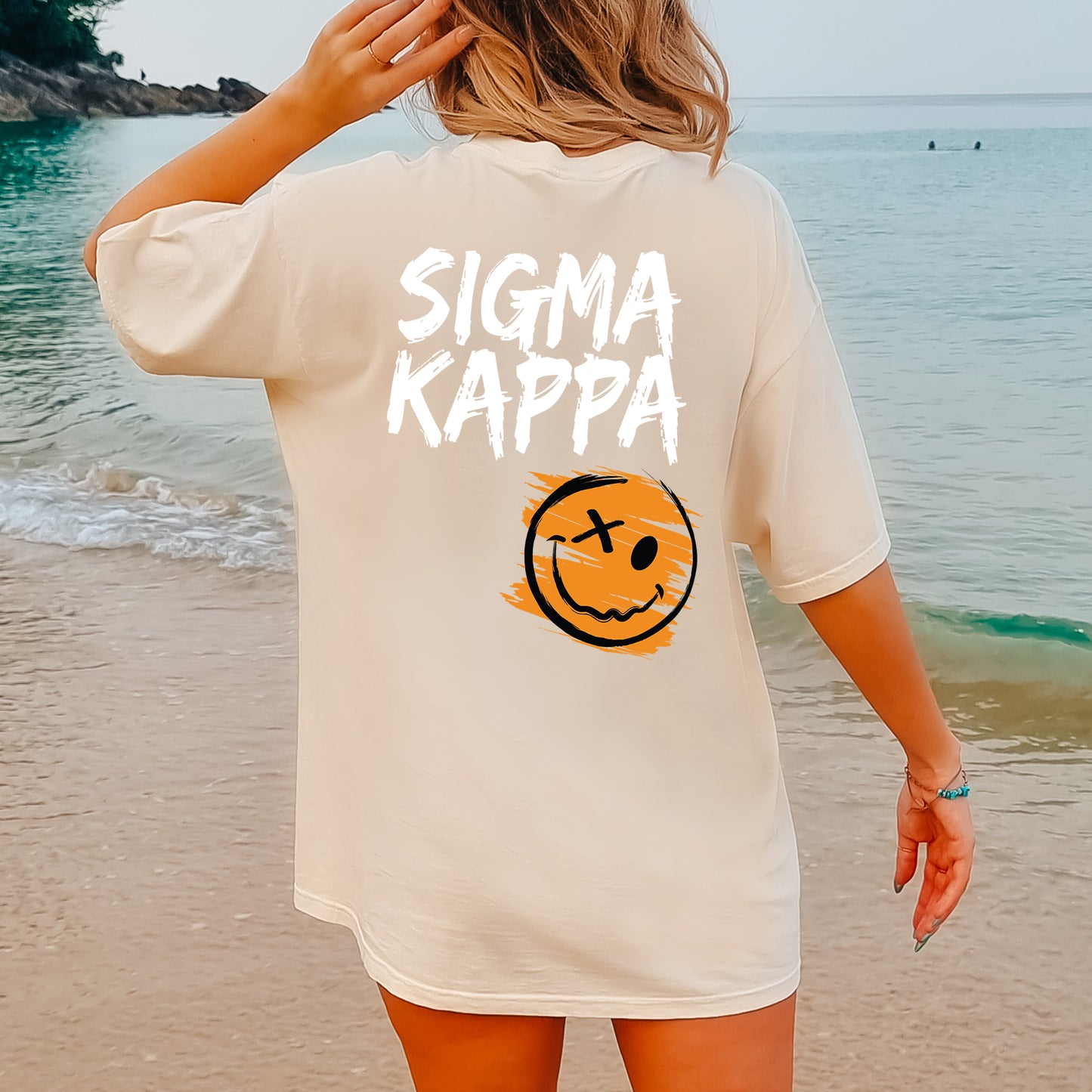 a woman standing on a beach wearing a shirt that says stigmaa kappa