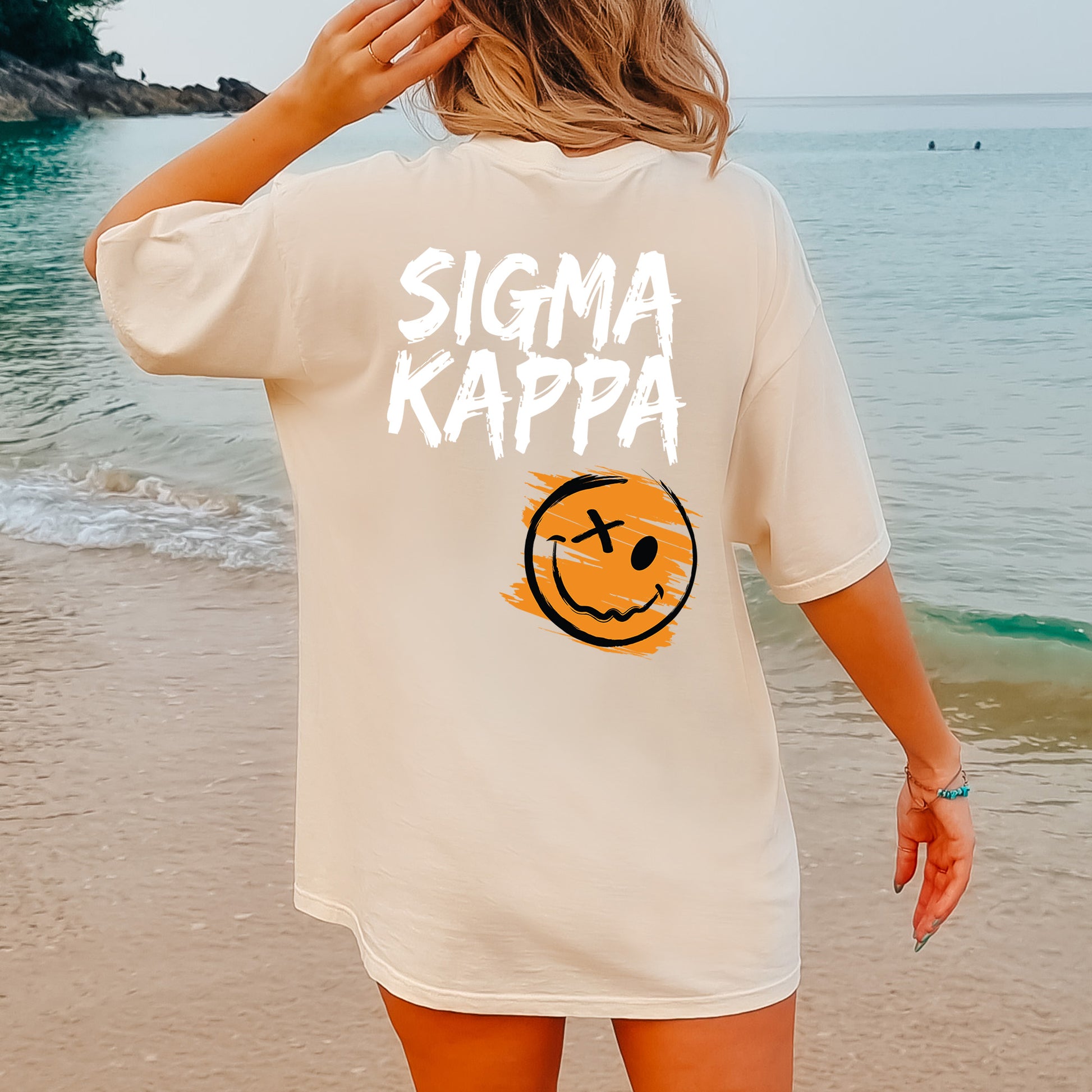 a woman standing on a beach wearing a shirt that says stigmaa kappa