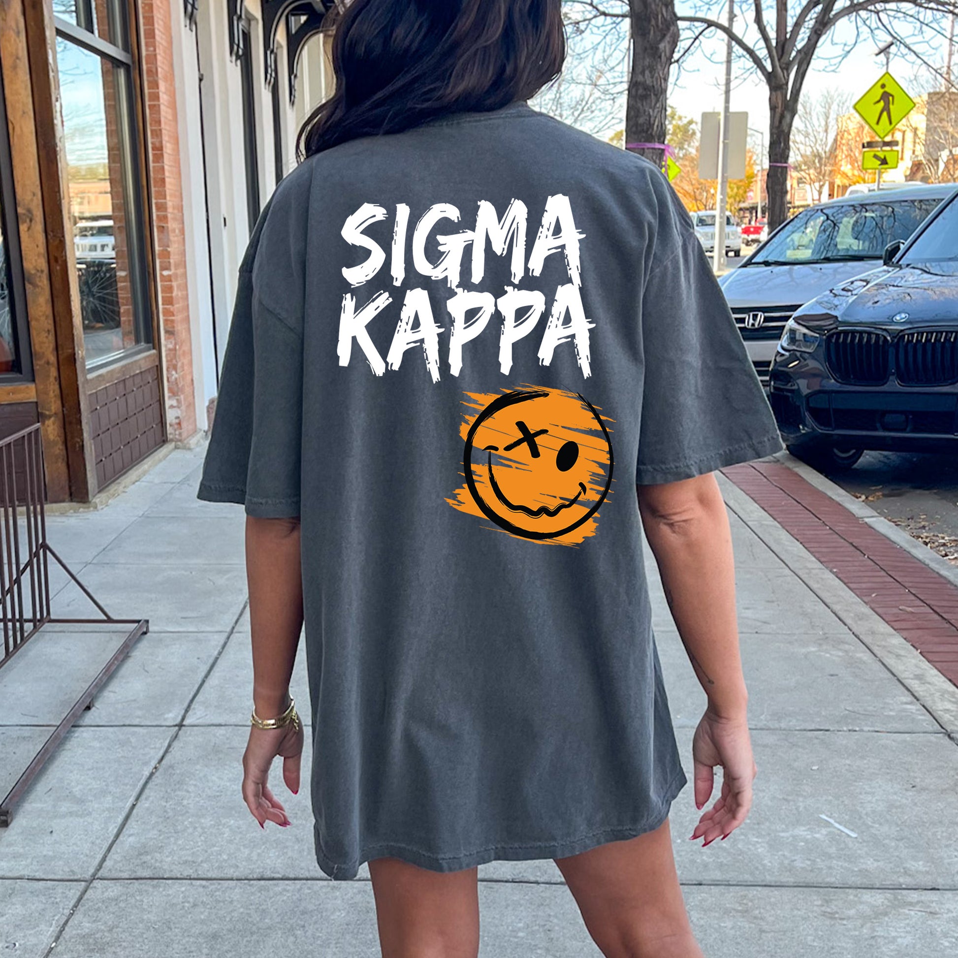 a woman walking down a sidewalk wearing a shirt that says stigmaa kappa