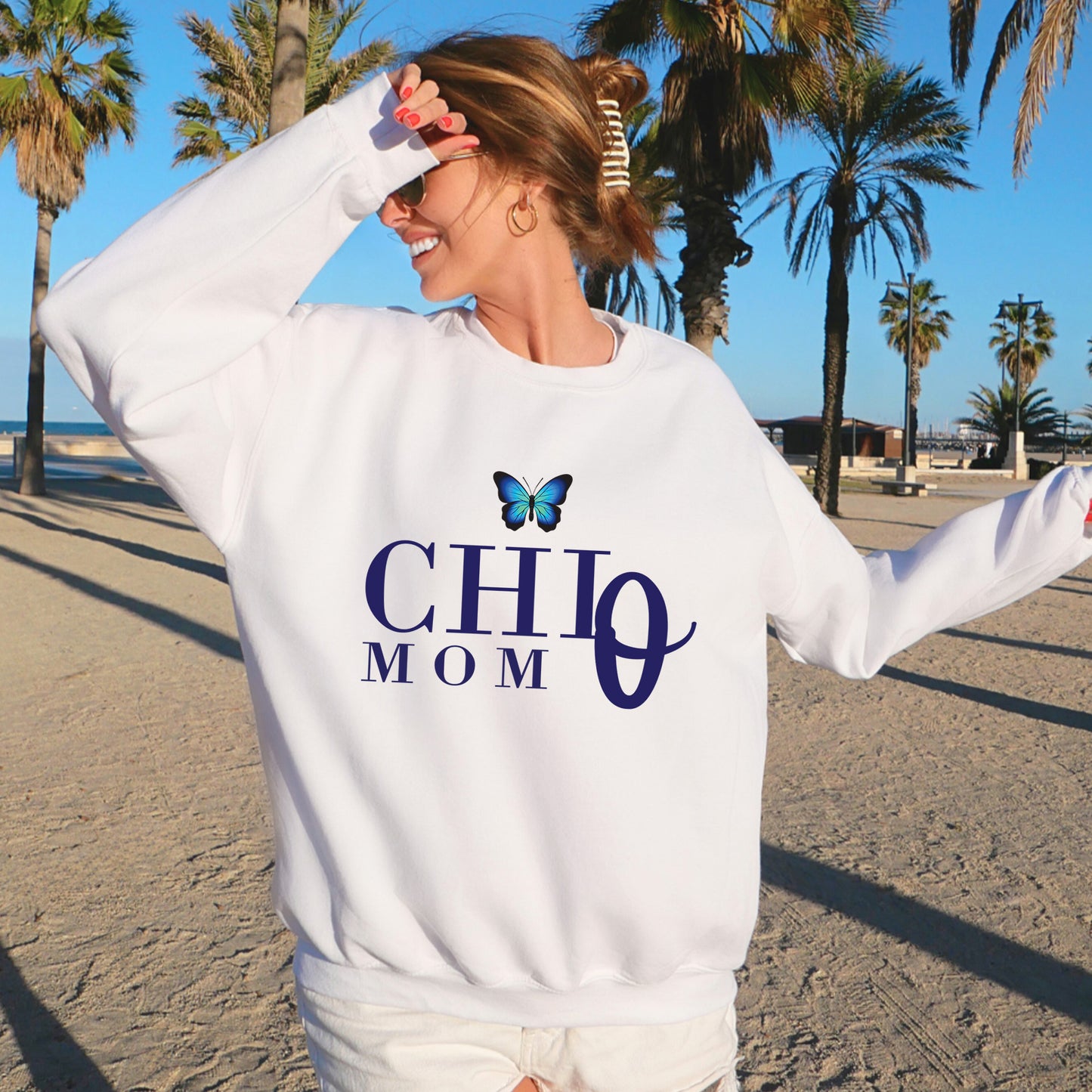 a woman standing on a beach wearing a white sweatshirt