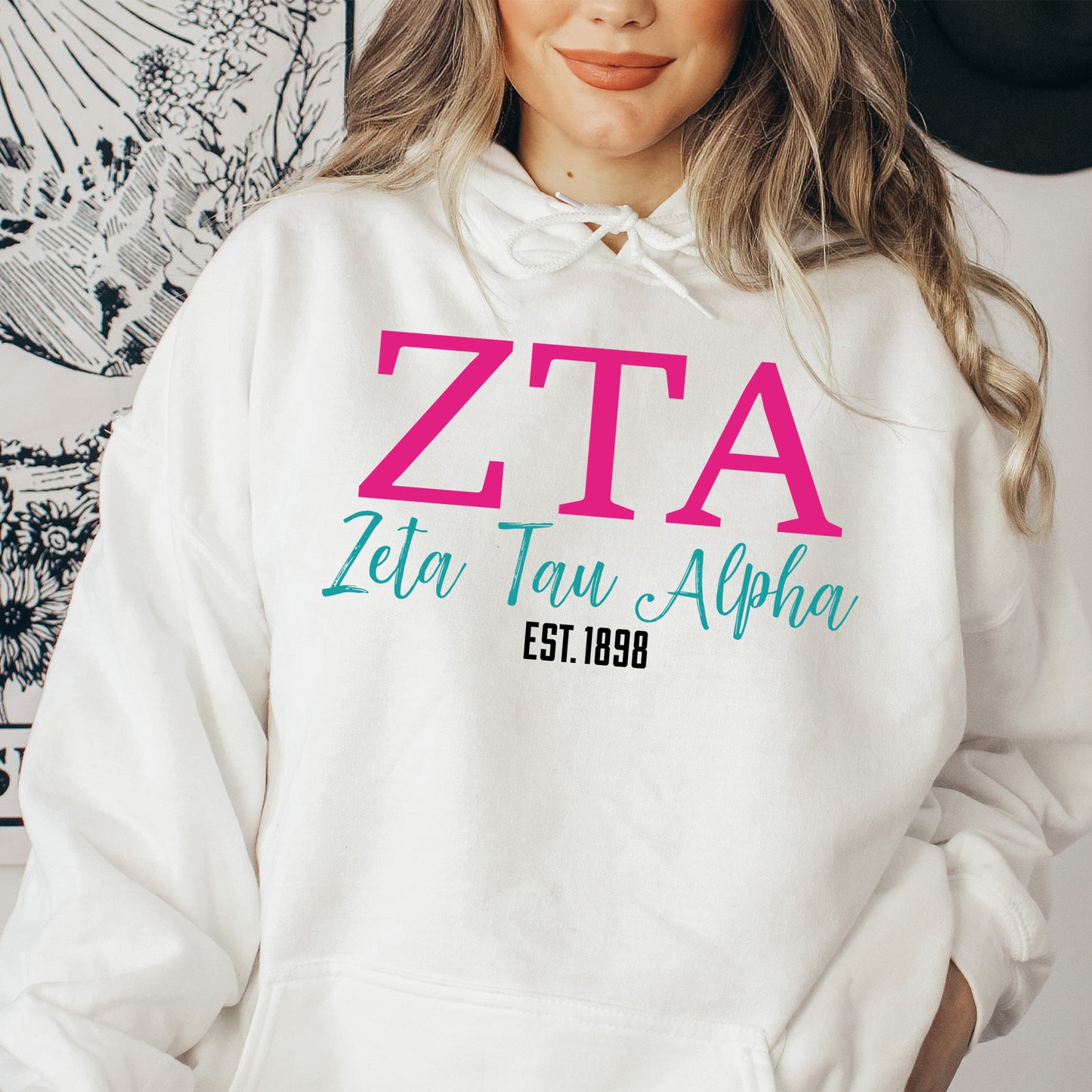a woman wearing a white hoodie with a pink zita on it