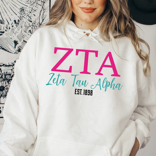 a woman wearing a white hoodie with a pink zita on it