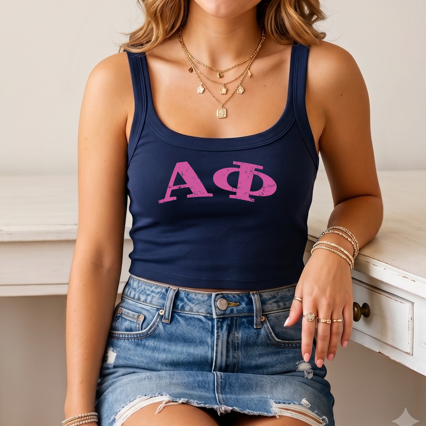 A woman wearing a navy blue crop top with the letters 'ΑΓΟ' printed on it, paired with a denim skirt and multiple rings on her fingers.