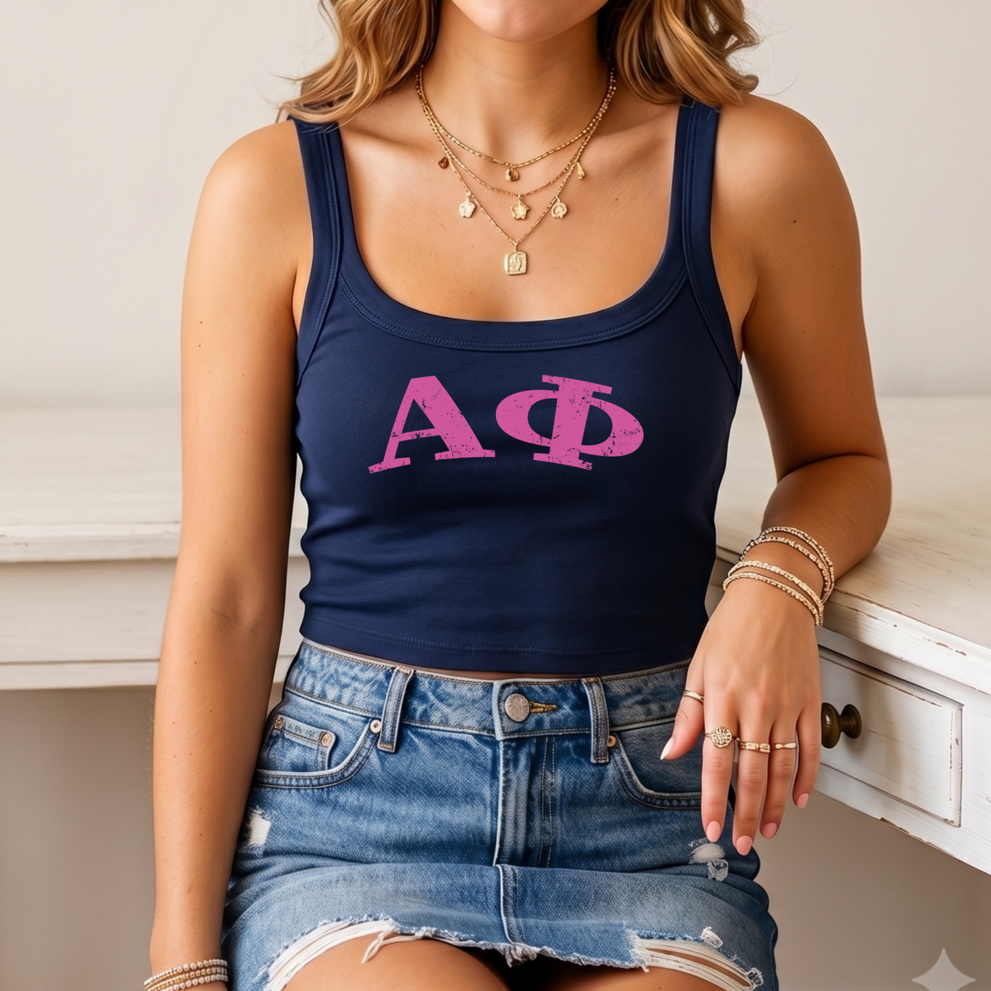 A woman wearing a navy blue crop top with the letters 'ΑΓΟ' printed on it, paired with a denim skirt and multiple rings on her fingers.
