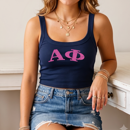 A woman wearing a navy blue crop top with the letters 'ΑΓΟ' printed on it, paired with a denim skirt and multiple rings on her fingers.