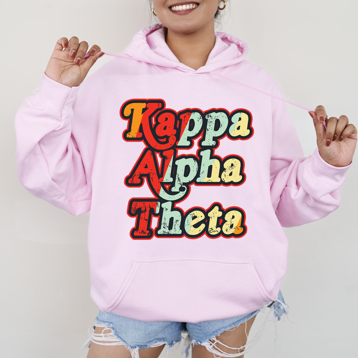 a woman wearing a pink hoodie that says kappa apha thea