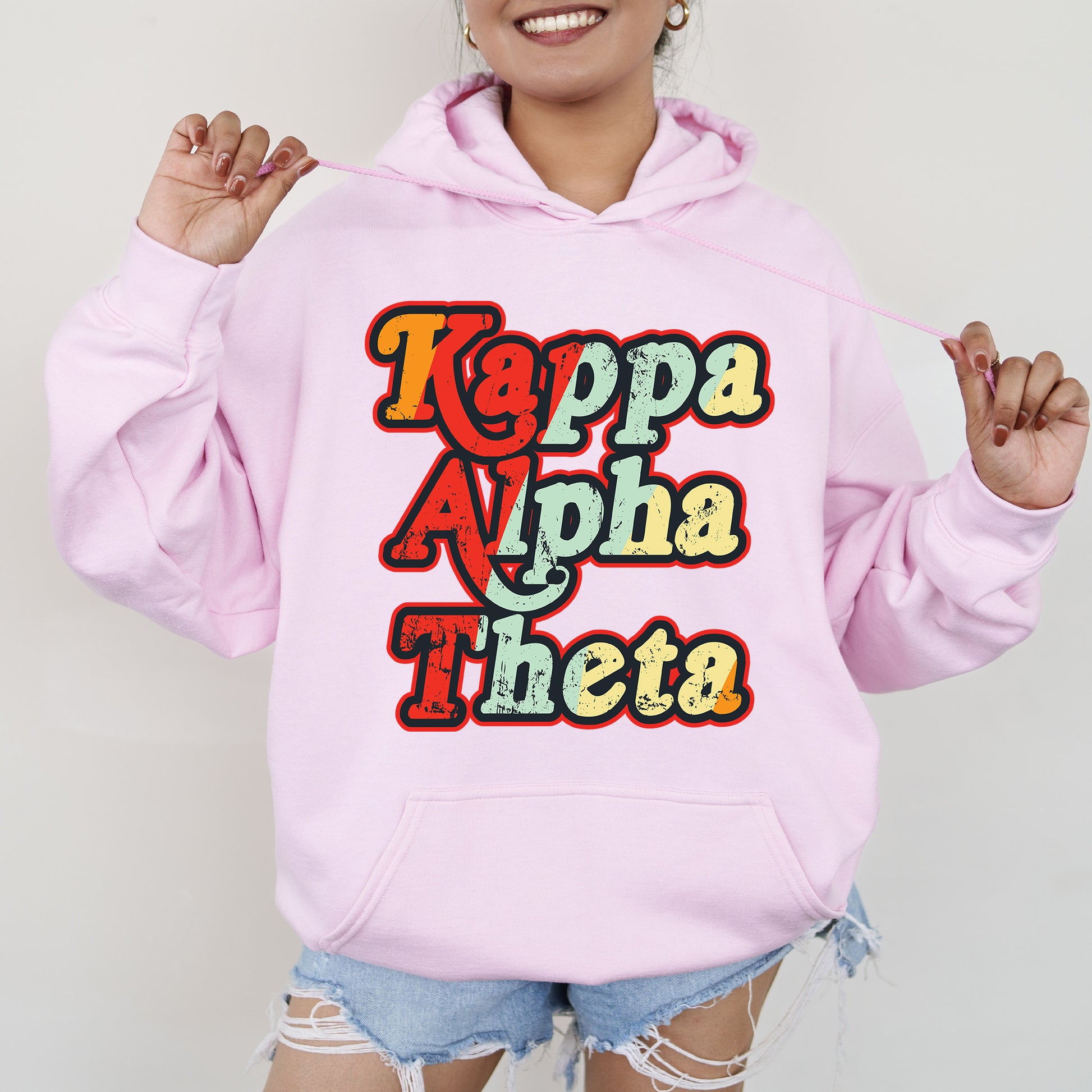 a woman wearing a pink hoodie that says kappa apha thea