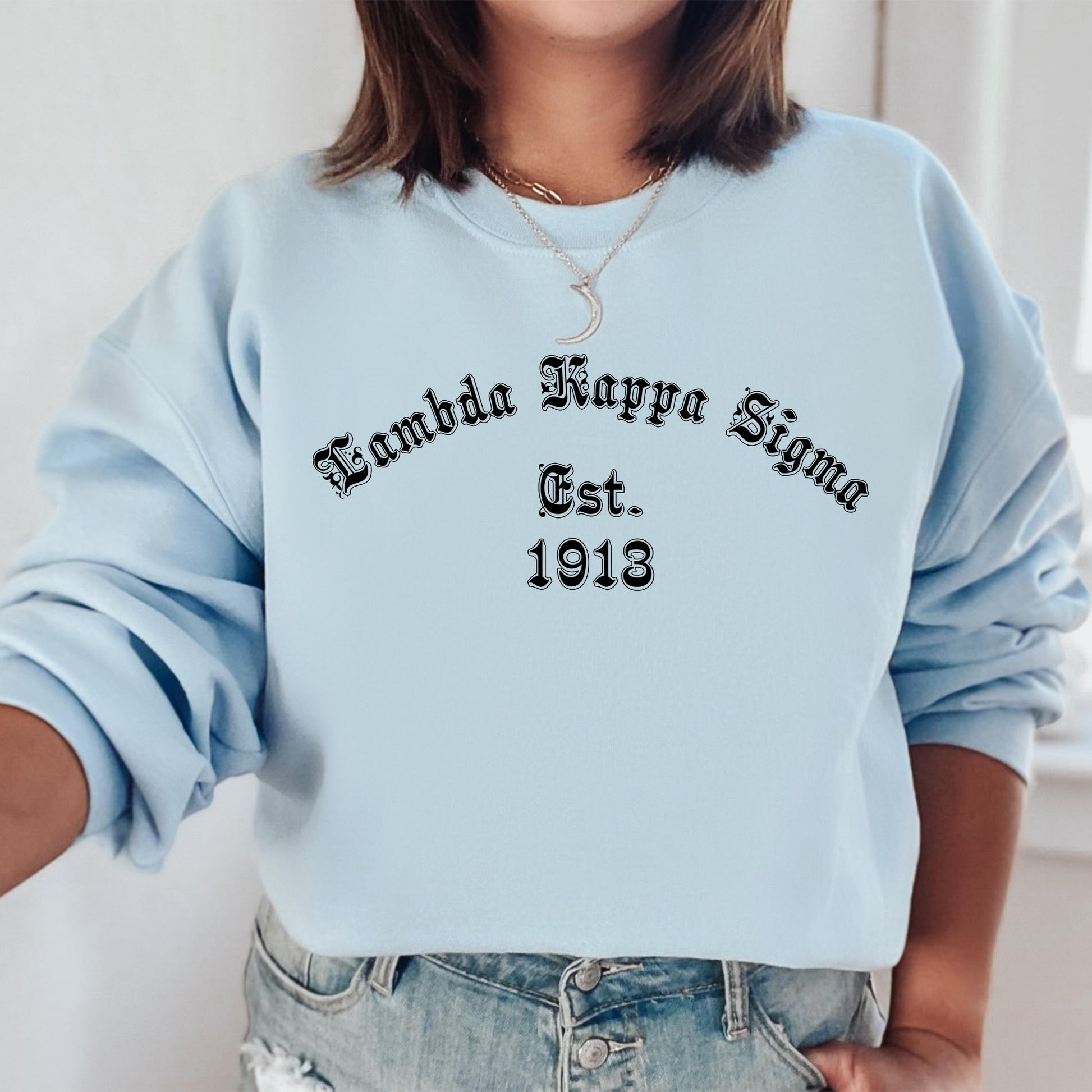a woman wearing a light blue sweatshirt with the words kanda karpa sing