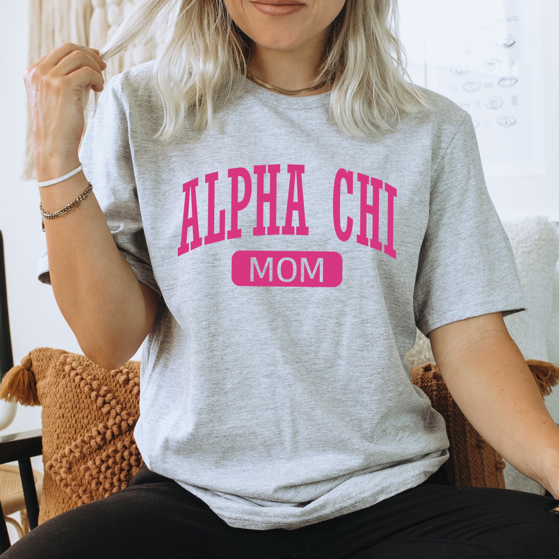 a woman sitting on a chair wearing a gray shirt with pink letters