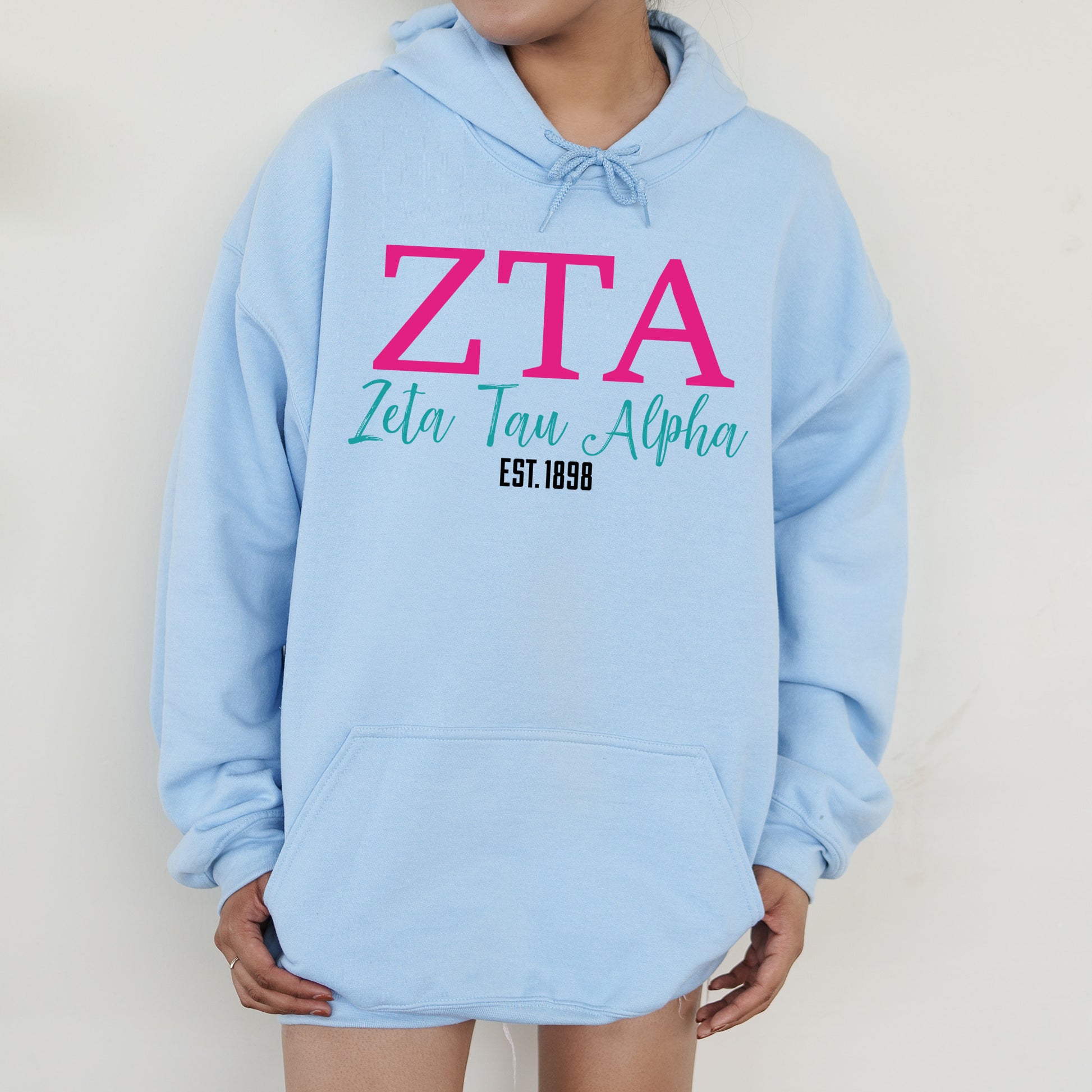 a woman wearing a blue hoodie with a pink and green zta on it