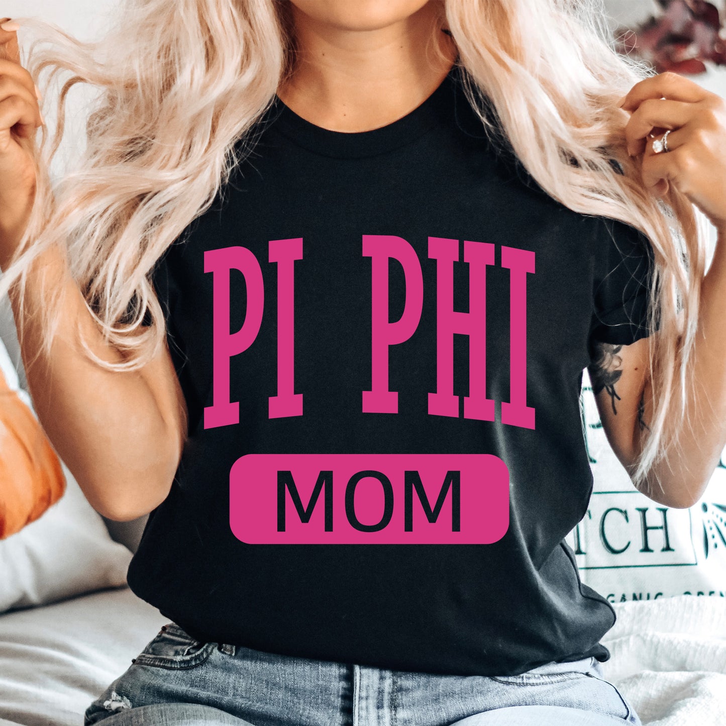 a woman sitting on a bed wearing a pi phi mom shirt