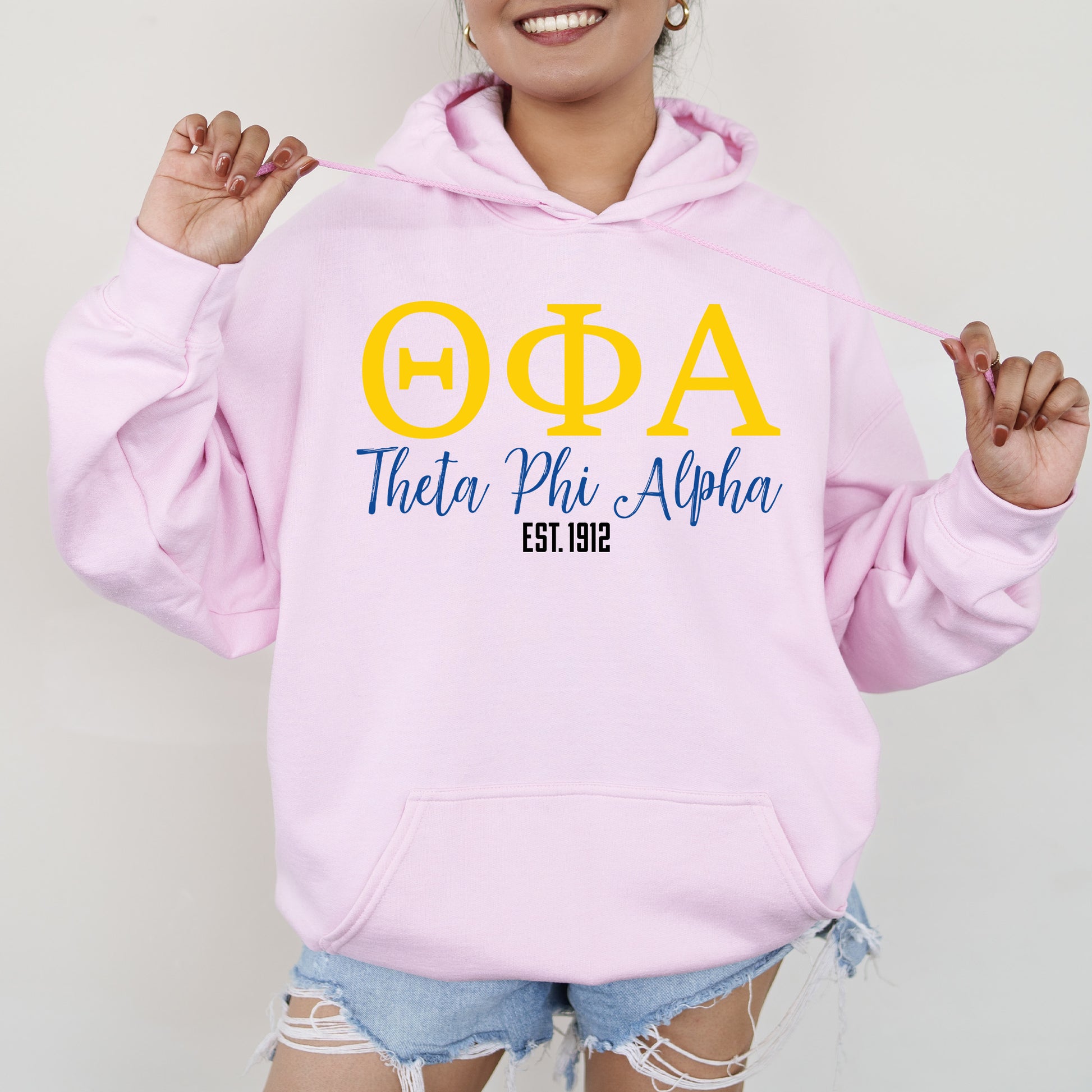 a woman wearing a pink hoodie with greek letters on it
