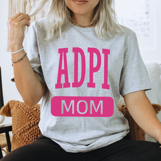 a woman sitting on a couch wearing a t - shirt that says adpi mom