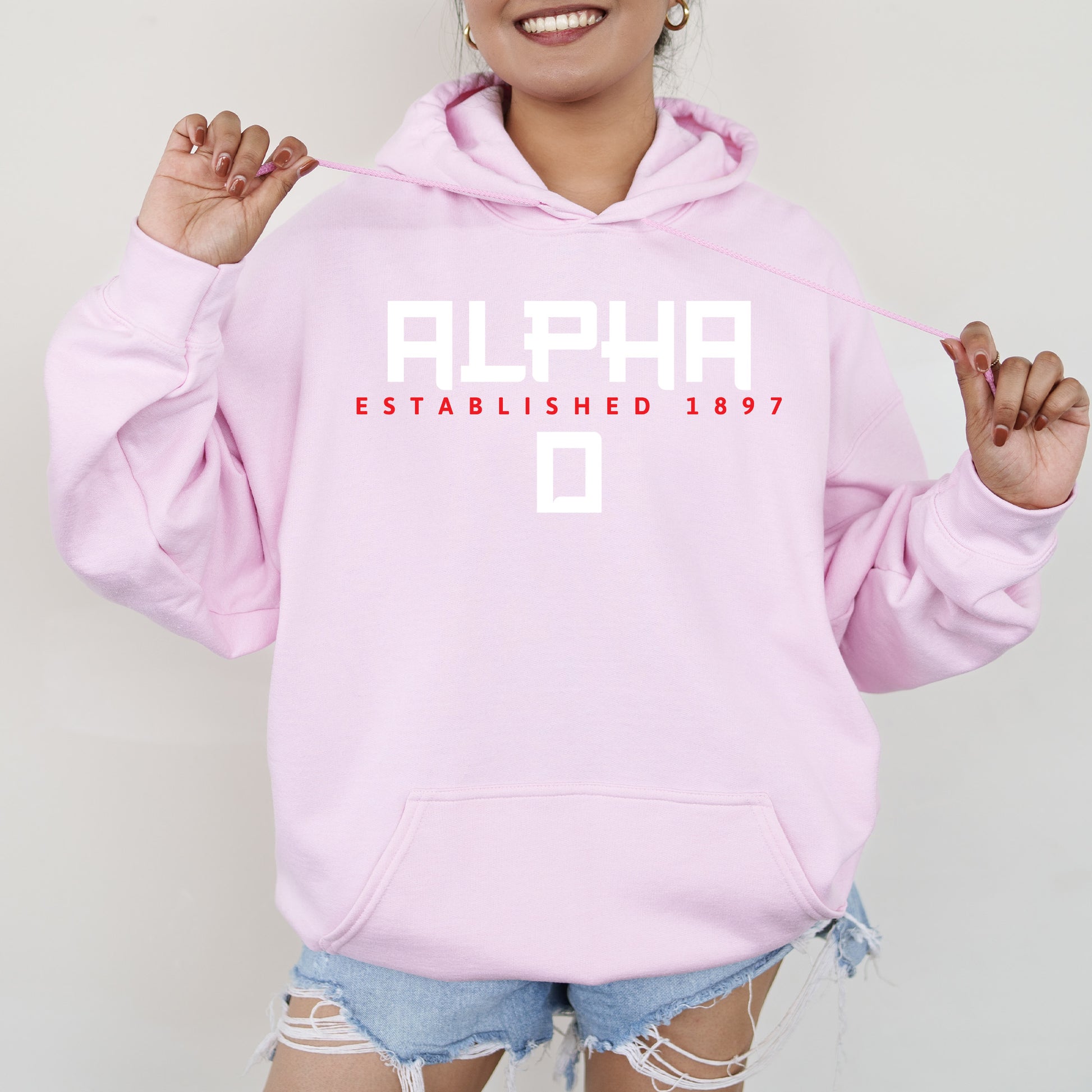 a woman wearing a pink hoodie that says alphon established 1897