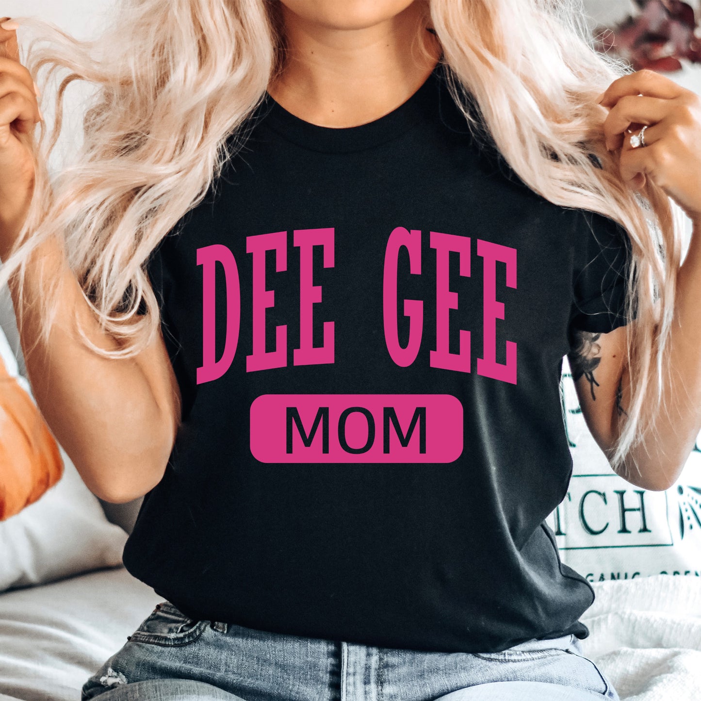a woman sitting on a bed wearing a t - shirt that says dee gee mom
