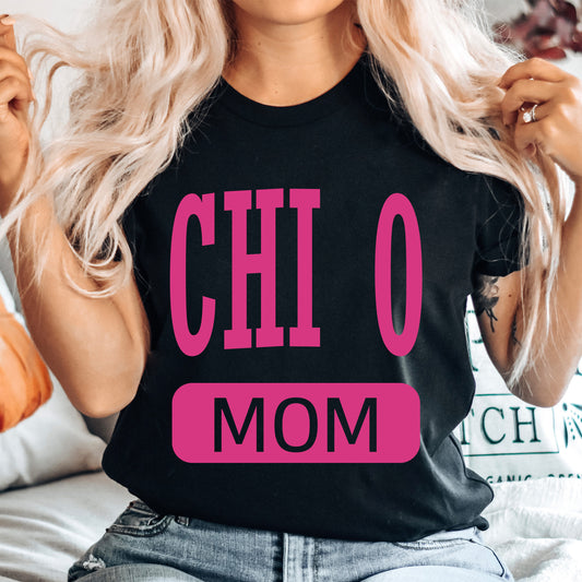 a woman sitting on a bed wearing a black shirt with pink letters