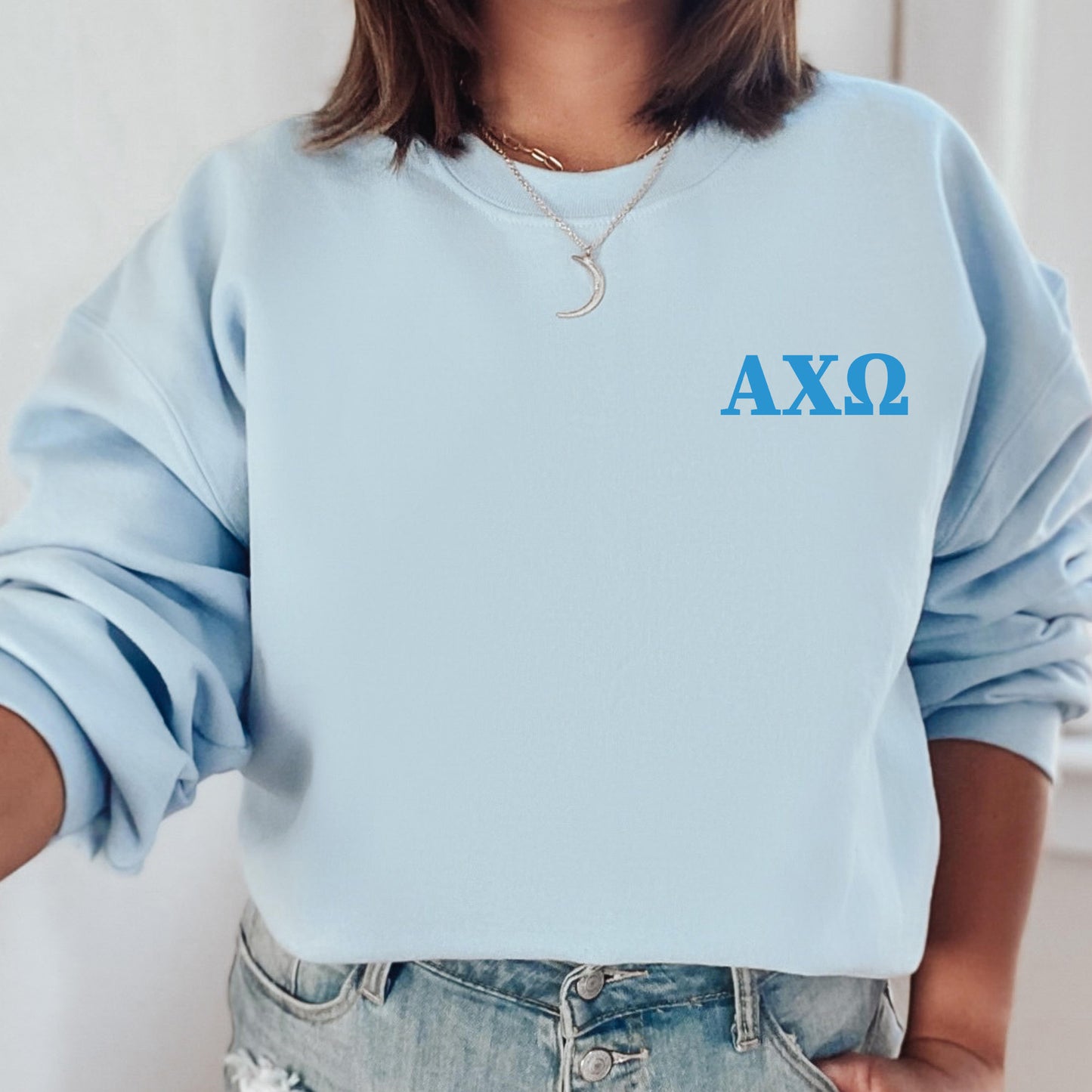a woman wearing a light blue sweatshirt with greek letters on it