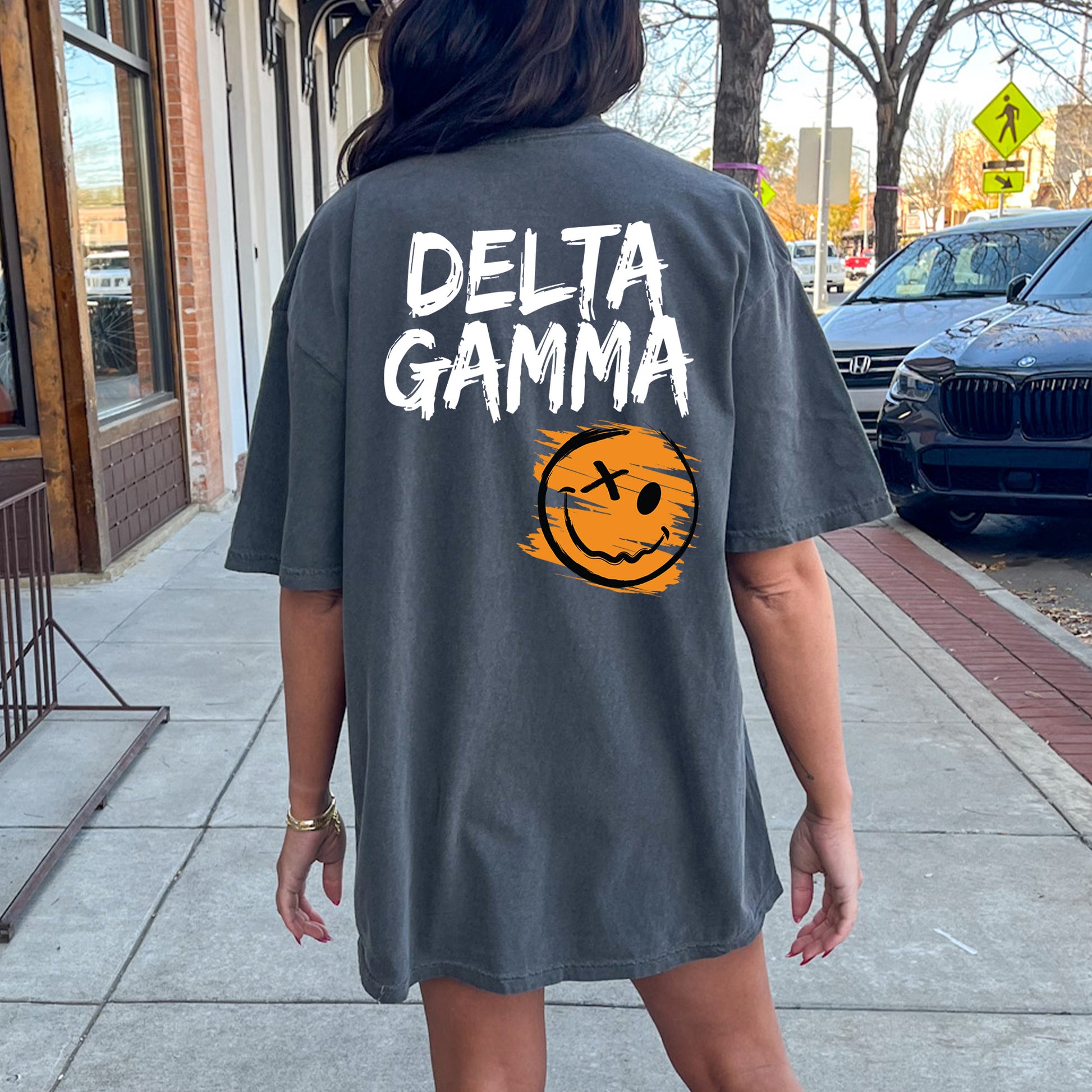 a woman walking down a sidewalk wearing a shirt that says delta gamma