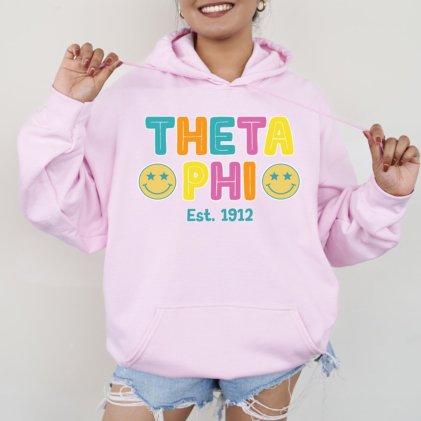 a woman wearing a pink hoodie that says thea phi est 1932