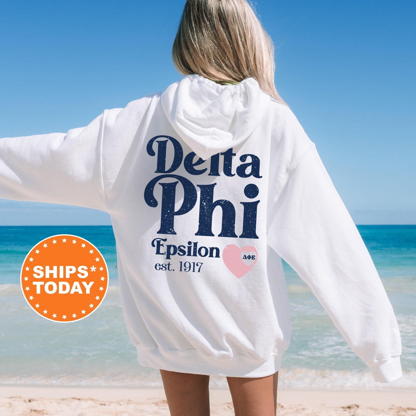 a woman standing on a beach wearing a white sweatshirt