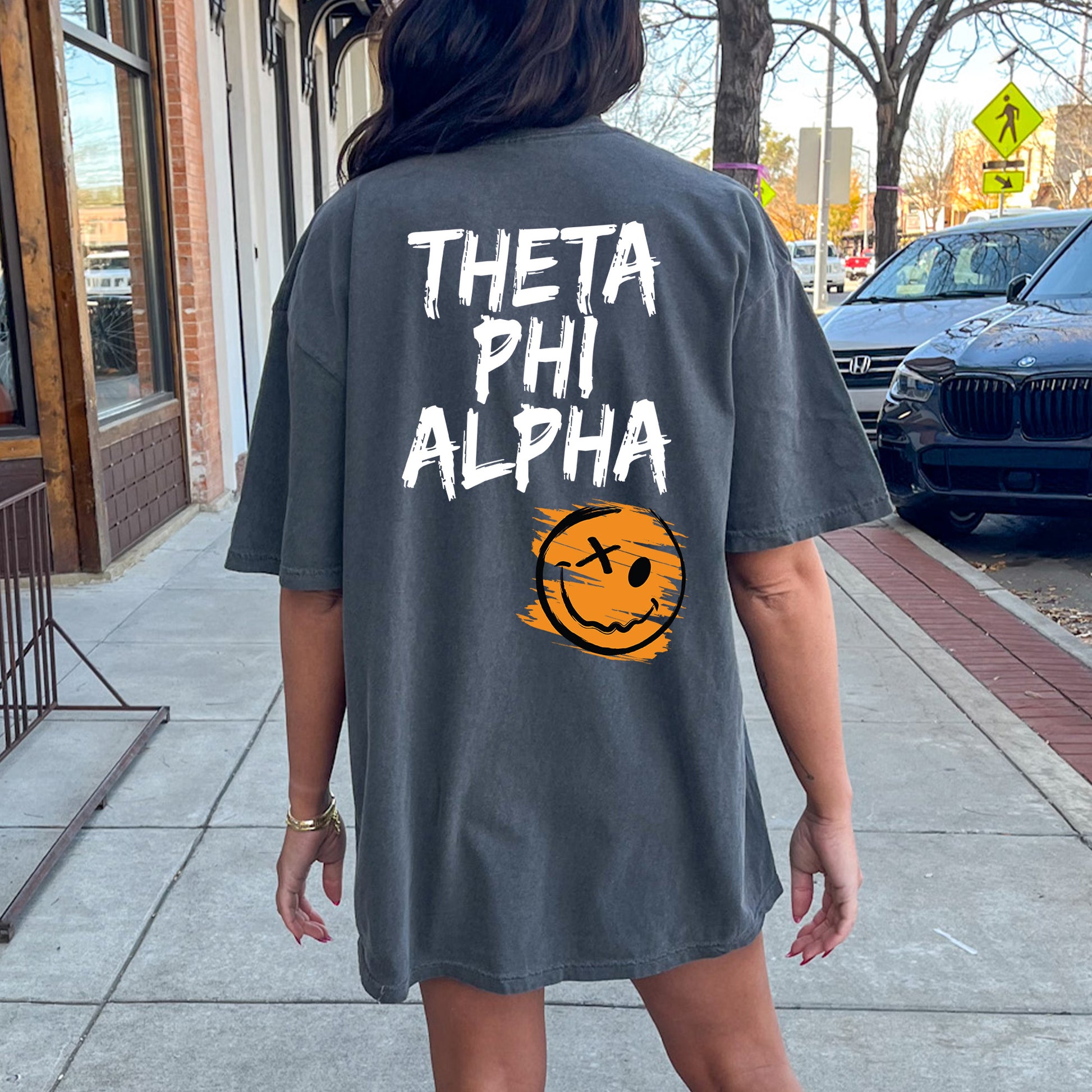 a woman walking down a sidewalk wearing a shirt that says, thea phi al