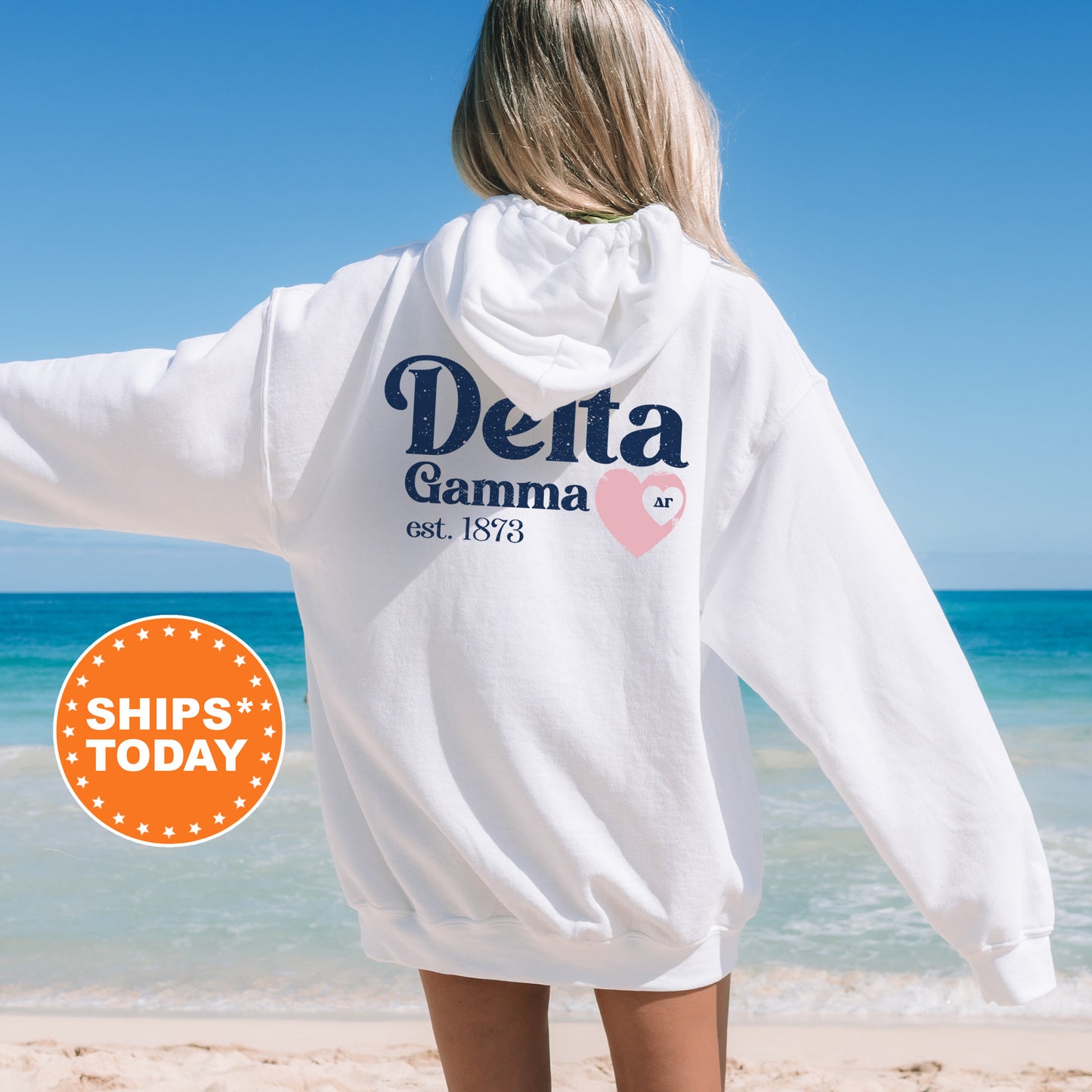 a woman standing on a beach wearing a white sweatshirt