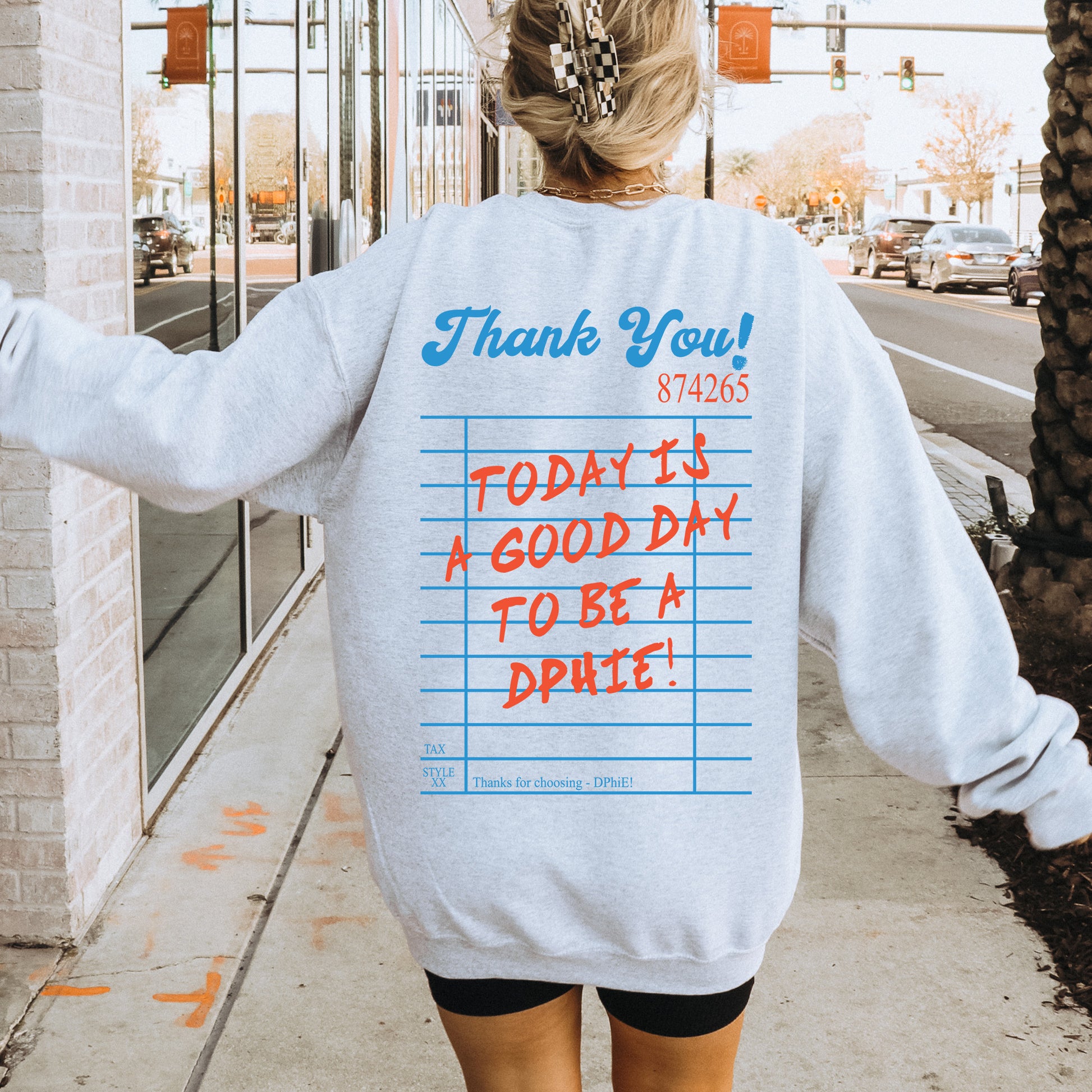 a woman walking down a sidewalk wearing a sweatshirt with writing on it