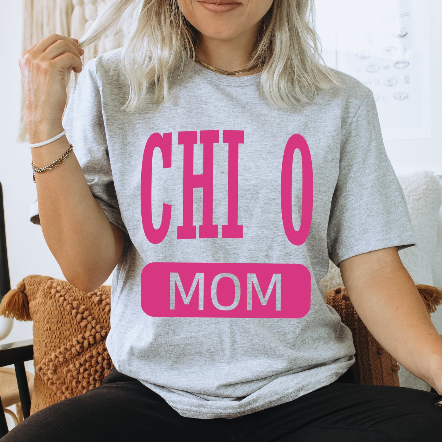 a woman sitting on a couch wearing a t - shirt that says chi 0 mom