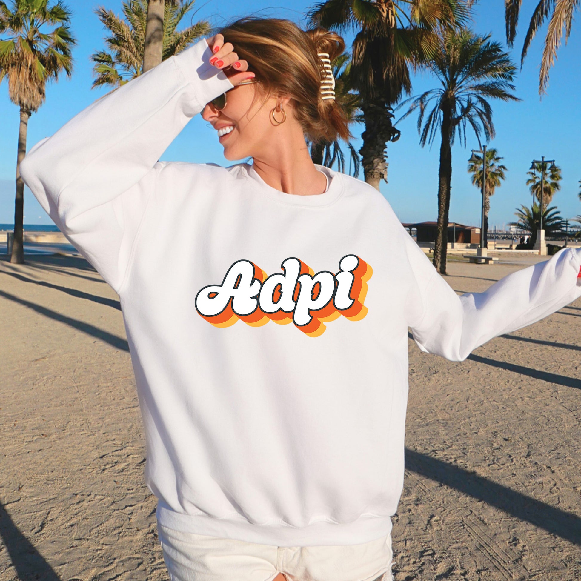 a woman standing on a beach wearing a white sweatshirt
