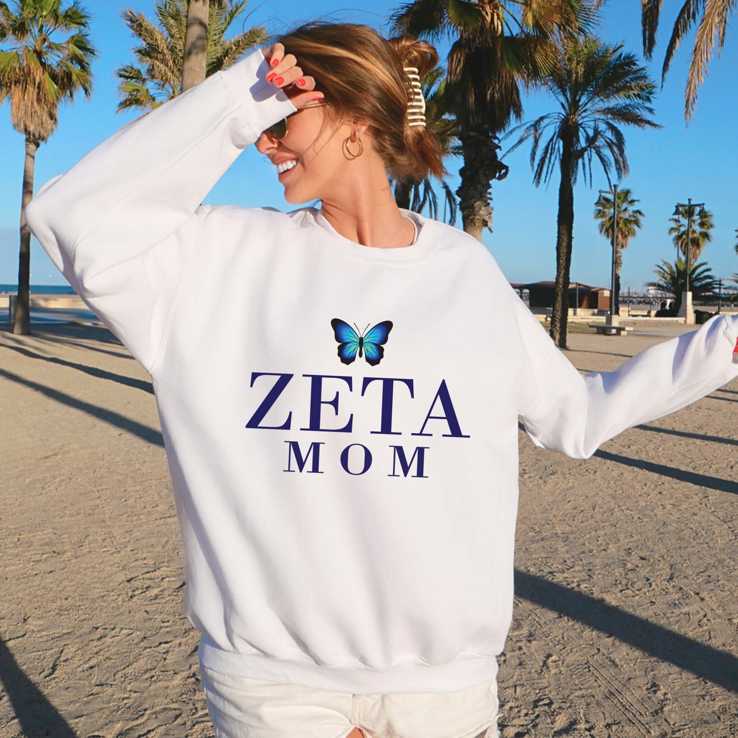 a woman standing on a beach wearing a sweatshirt that says zeta mom