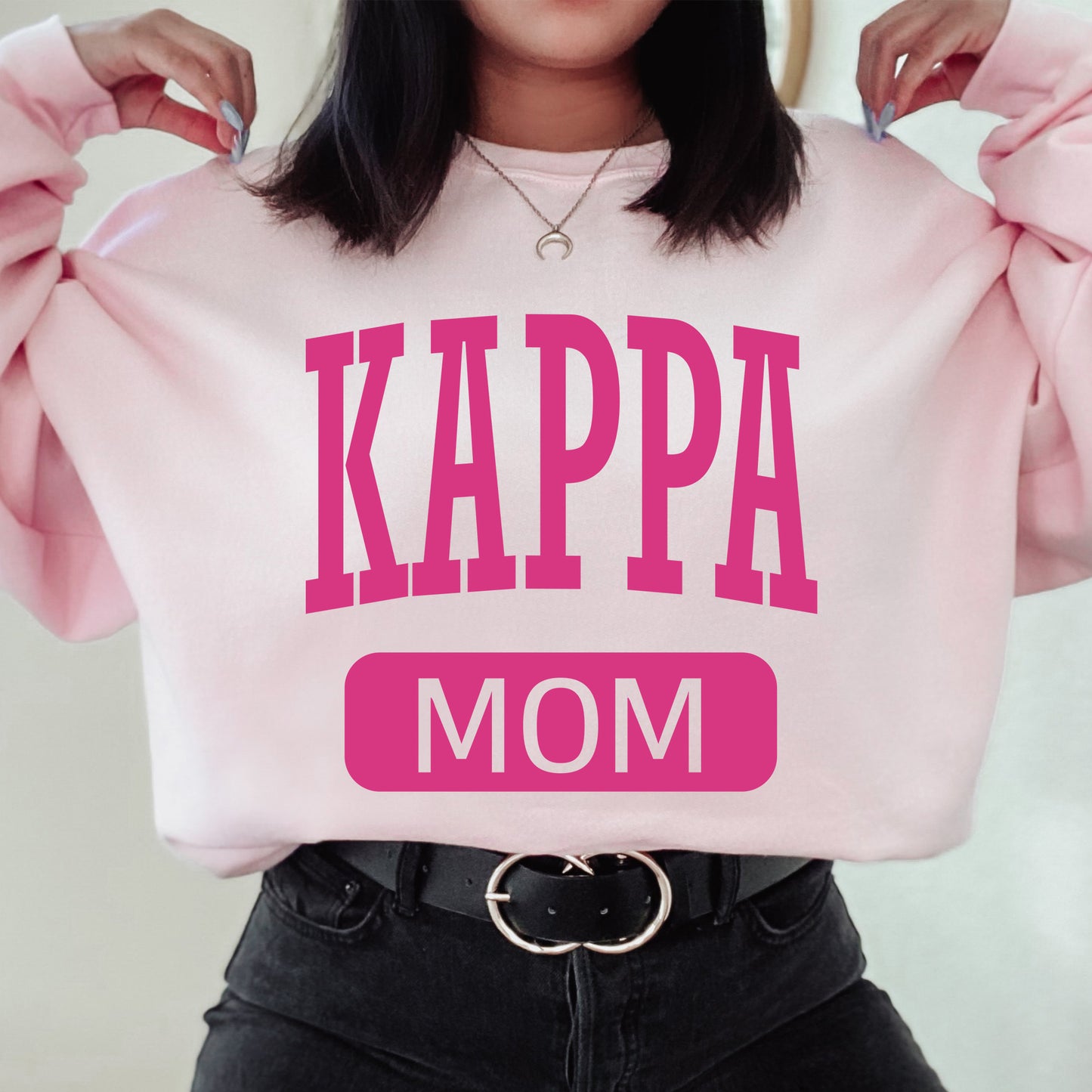 a woman wearing a pink sweatshirt that says kappa mom