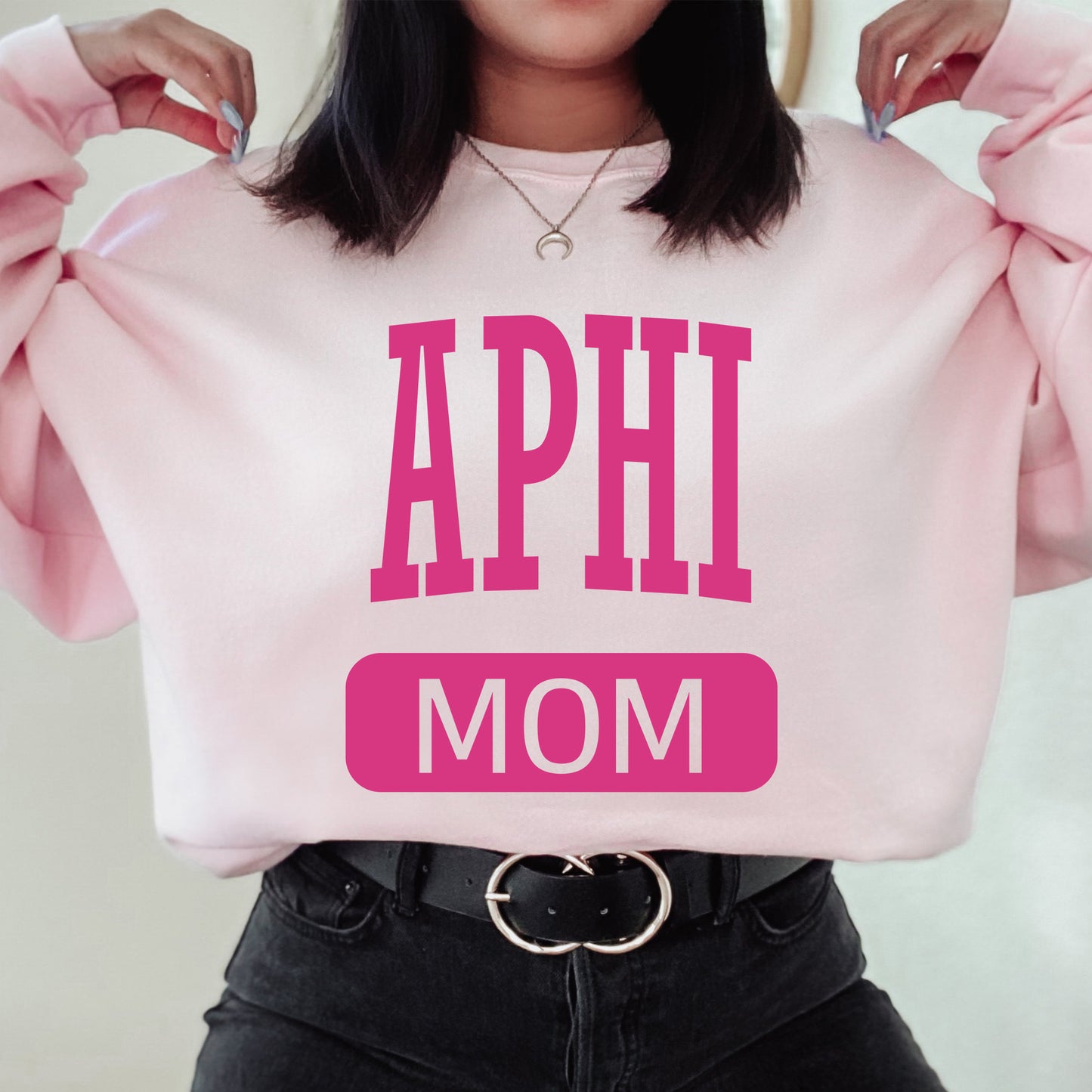 a woman wearing a pink sweatshirt with the words aphi mom on it