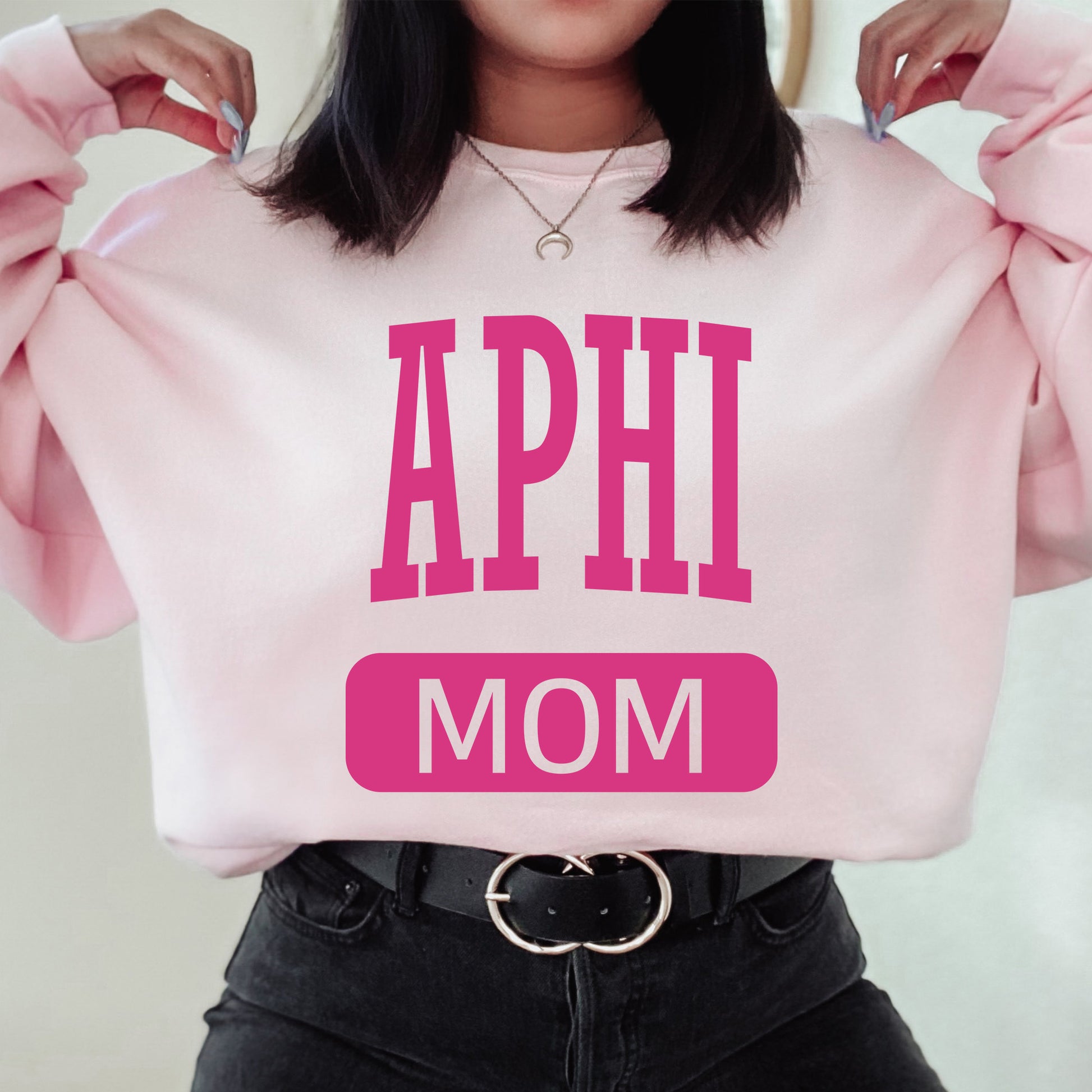 a woman wearing a pink sweatshirt with the words aphi mom on it
