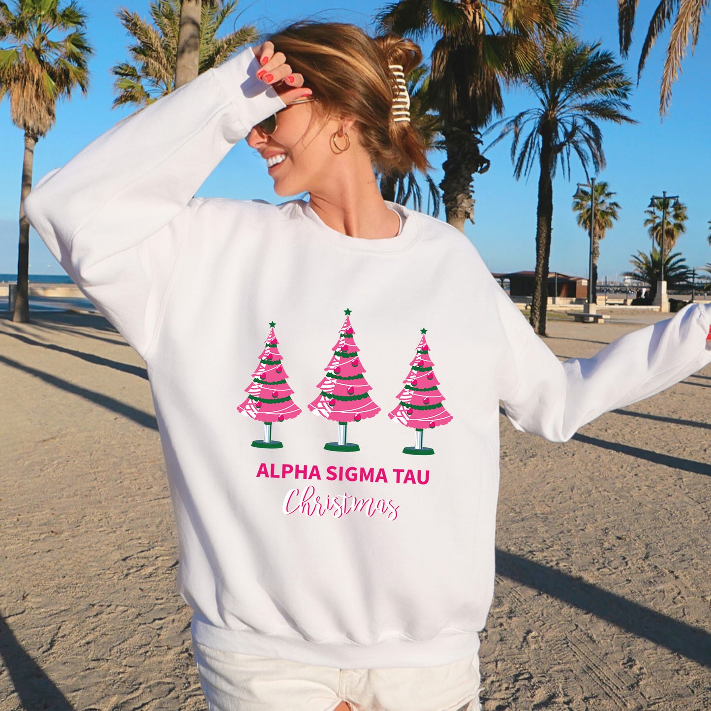 a woman standing on a beach wearing a sweatshirt with christmas trees on it