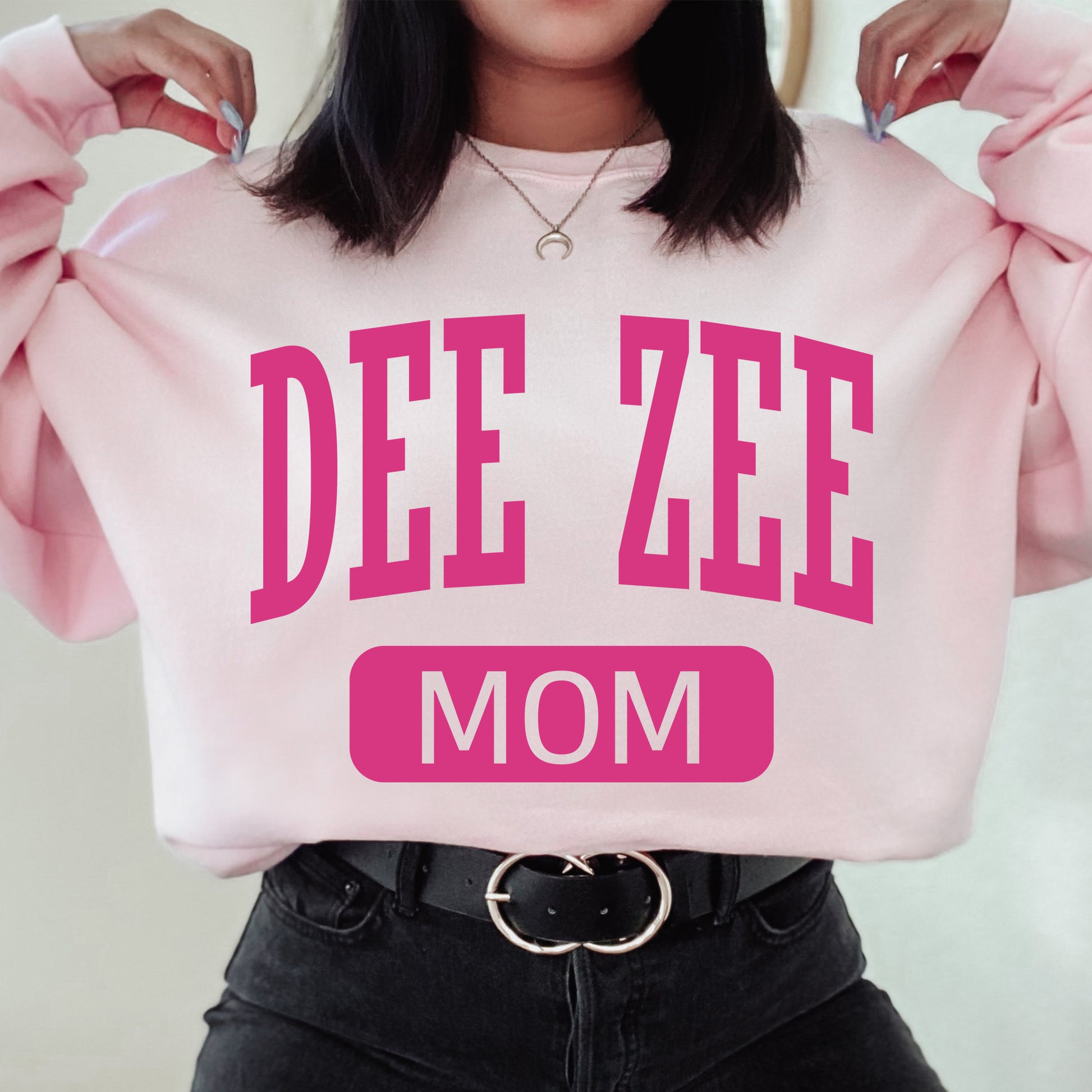 a woman wearing a pink sweatshirt that says dee zeee mom