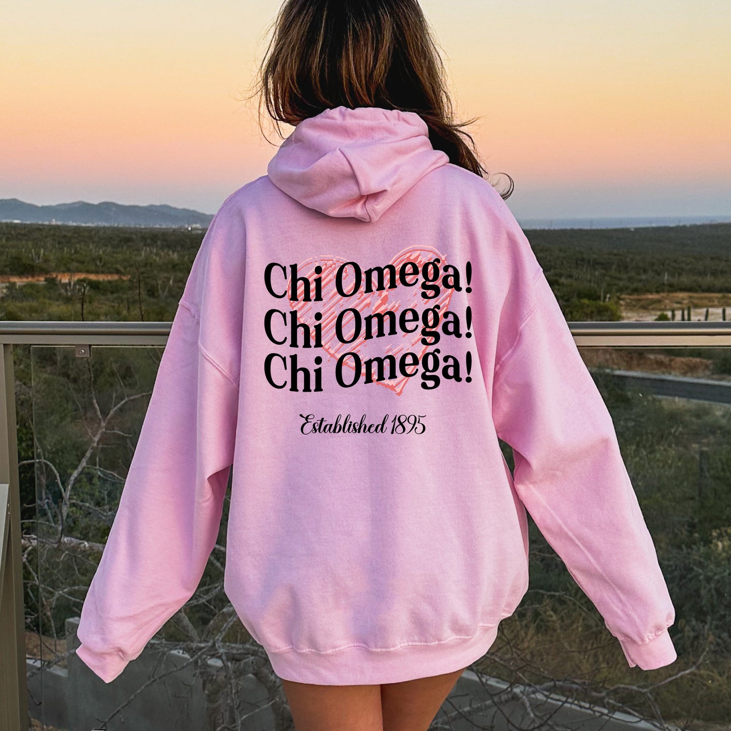 a woman wearing a pink hoodie with the words chi omega, chi