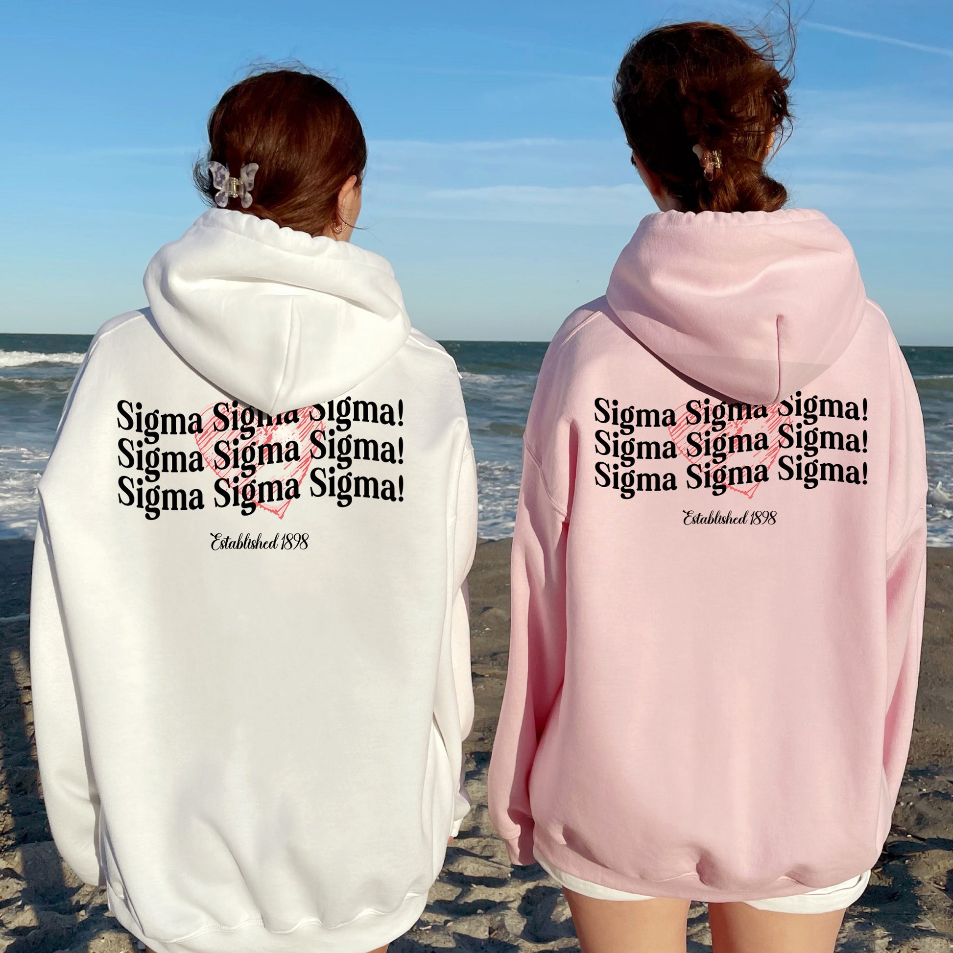 two people standing on a beach wearing matching sweatshirts