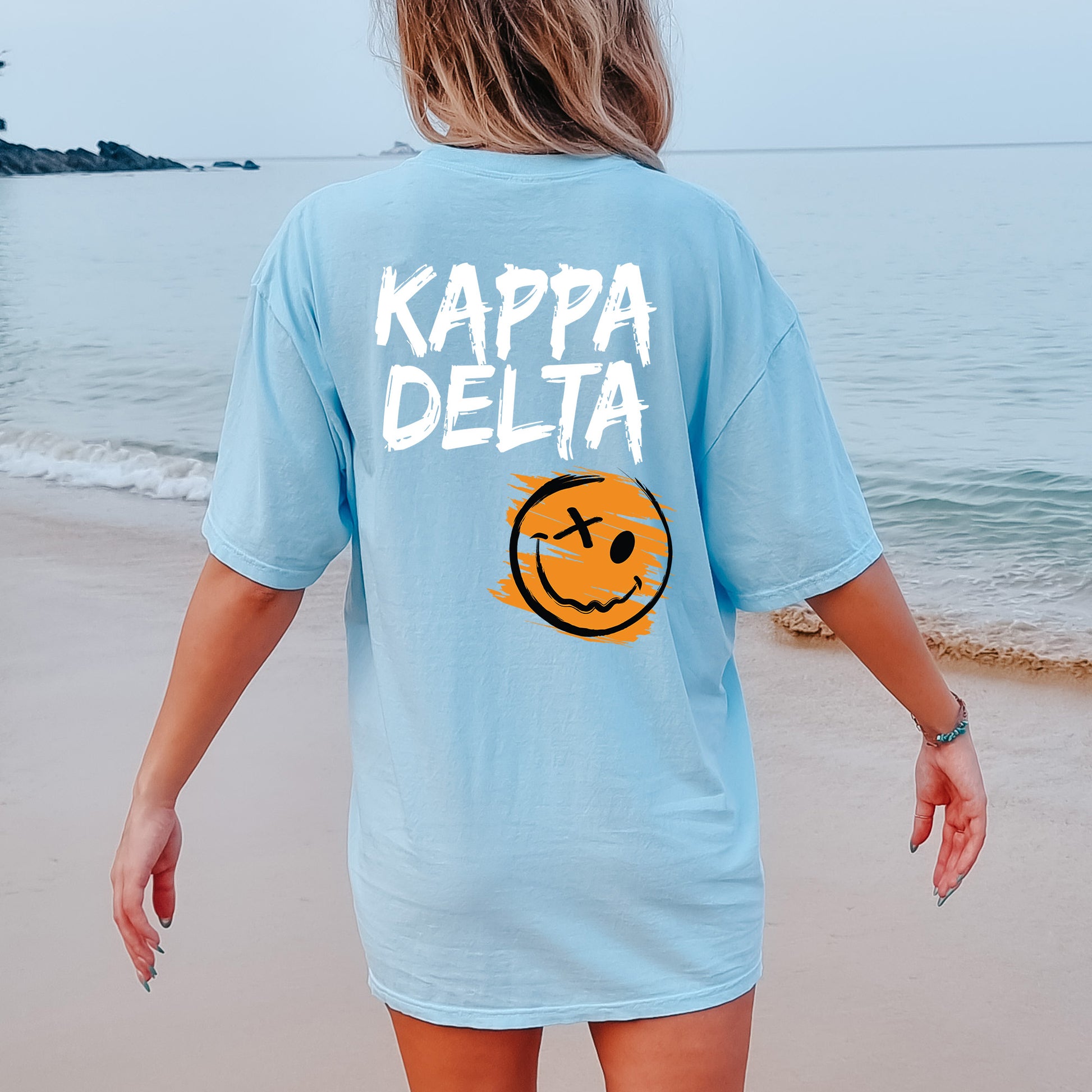 a woman walking on the beach with a smiley face on her shirt