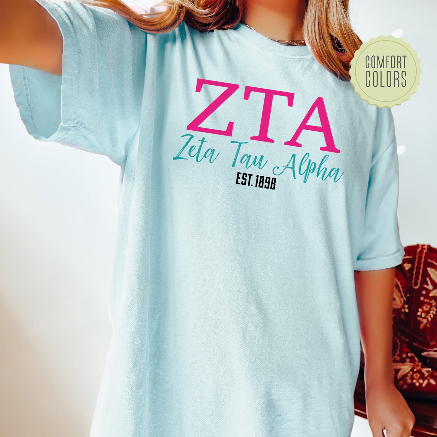 a woman wearing a blue t - shirt with a pink zta on it