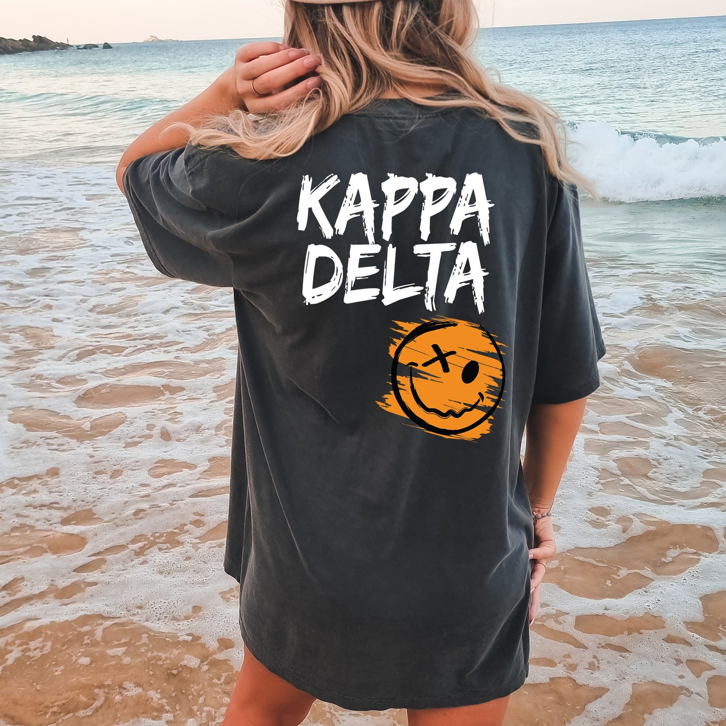 a woman standing on a beach wearing a black shirt that says kappa delta