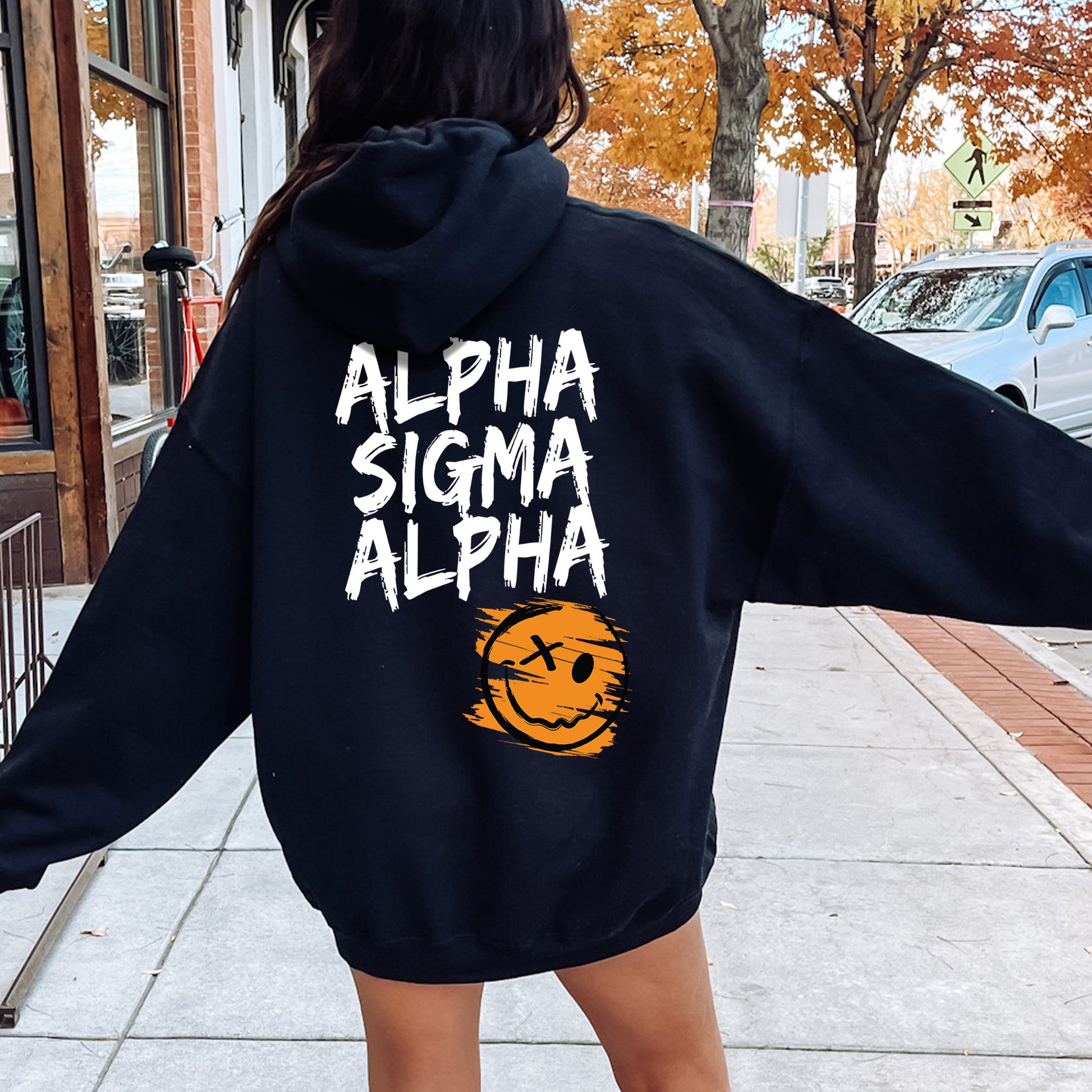 a woman walking down a sidewalk wearing a black hoodie