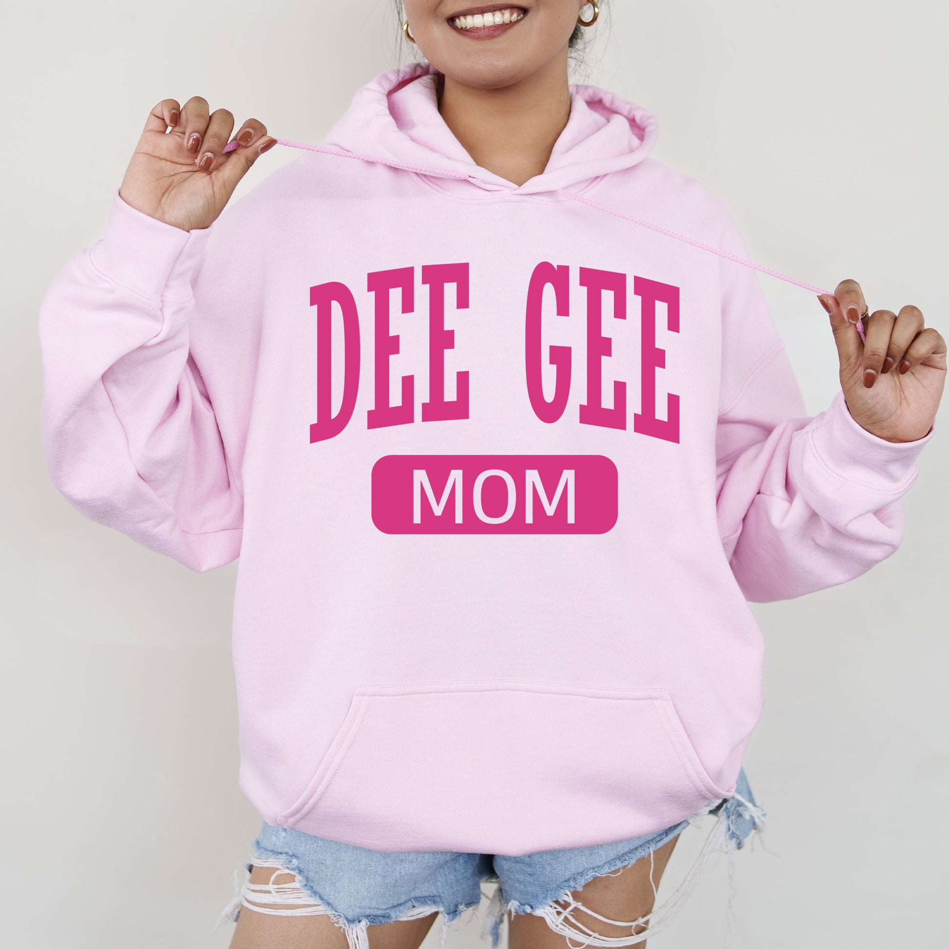 a woman wearing a pink hoodie that says dee gee mom