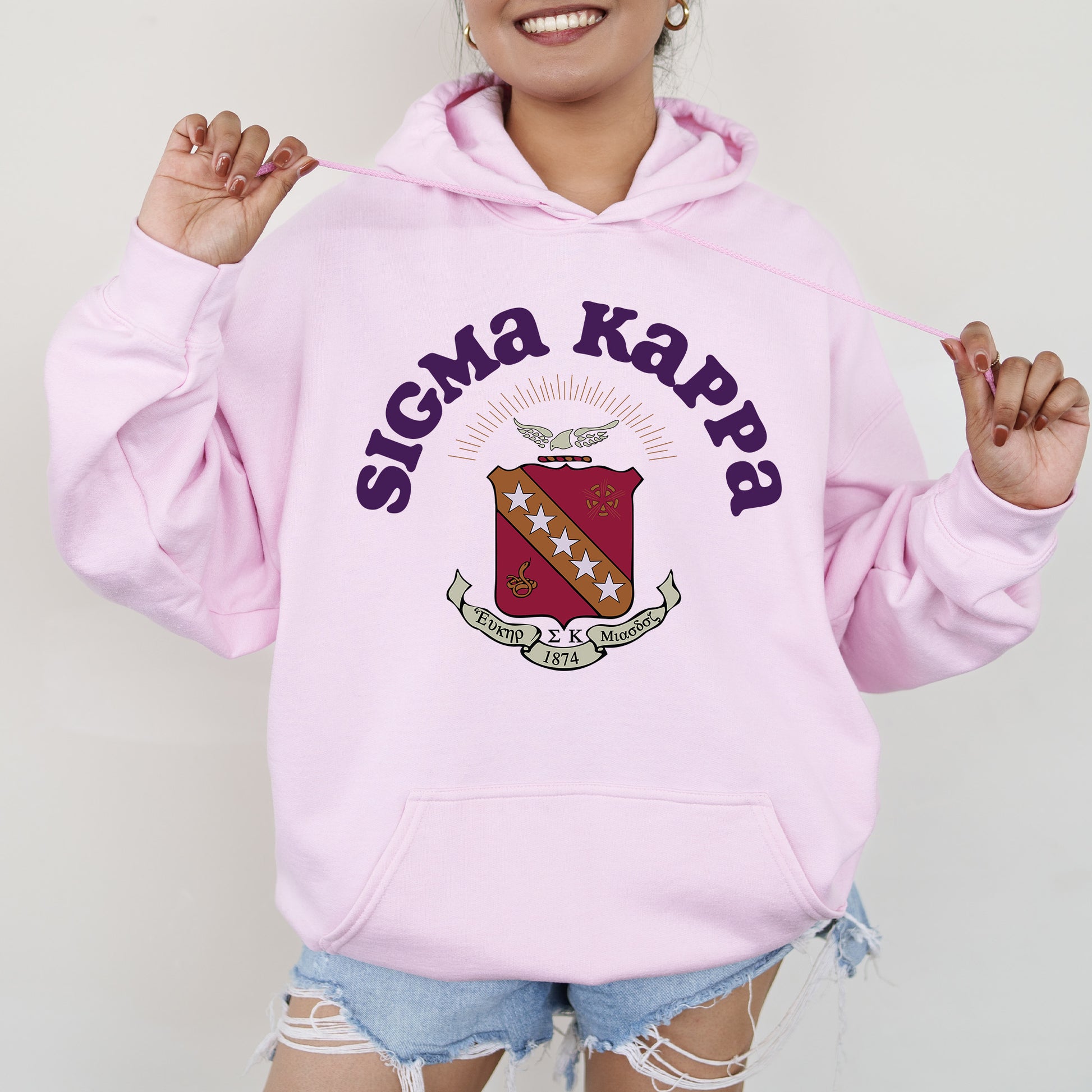 a woman wearing a pink hoodie with the words stigmana kapp on it