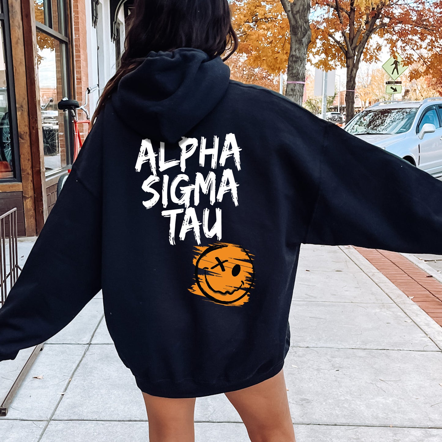 a woman walking down a sidewalk wearing a black hoodie